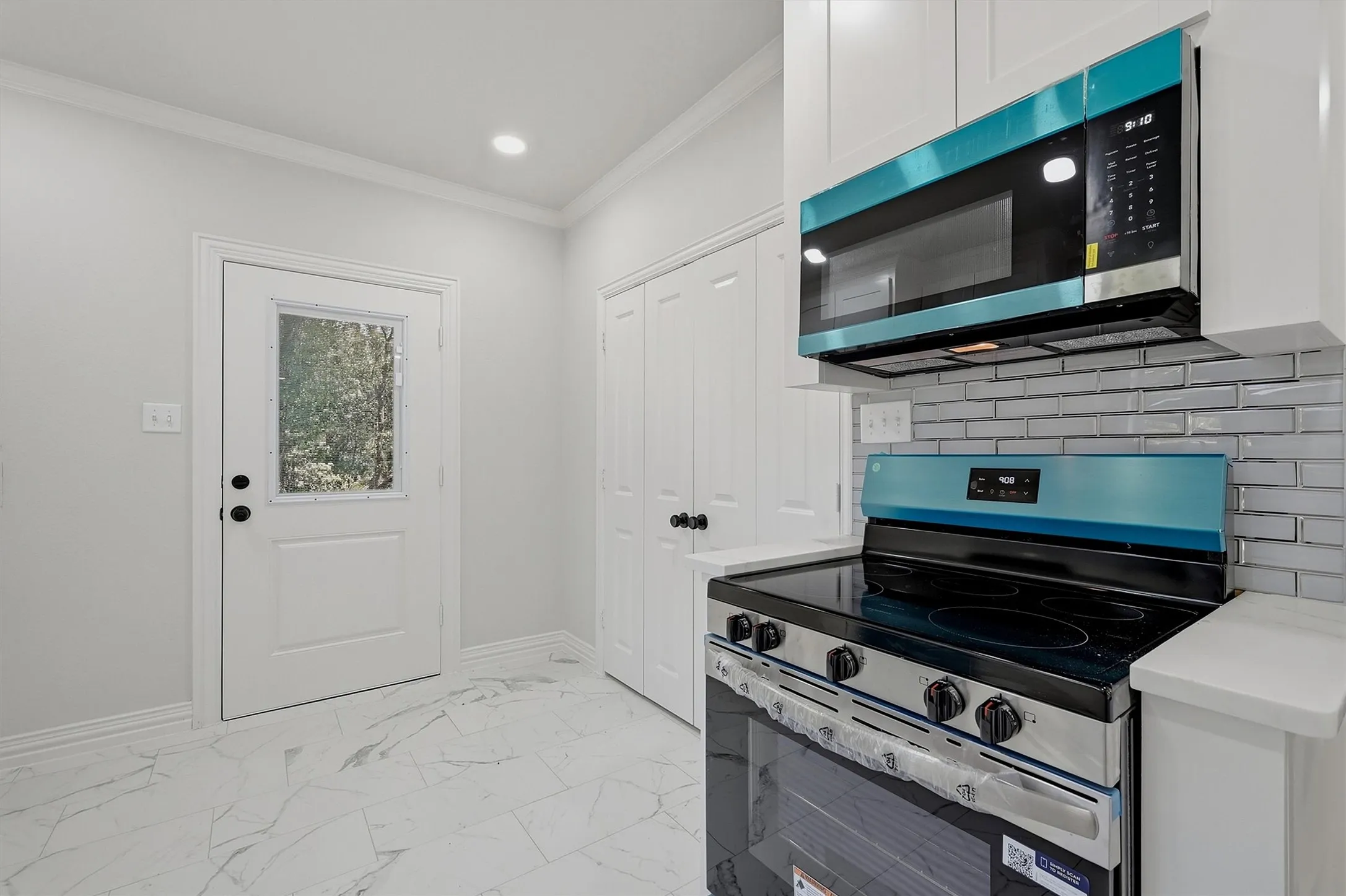 White shaker cabinetry, subway tile backsplash, stainless steel range and microwave, and white tile flooring