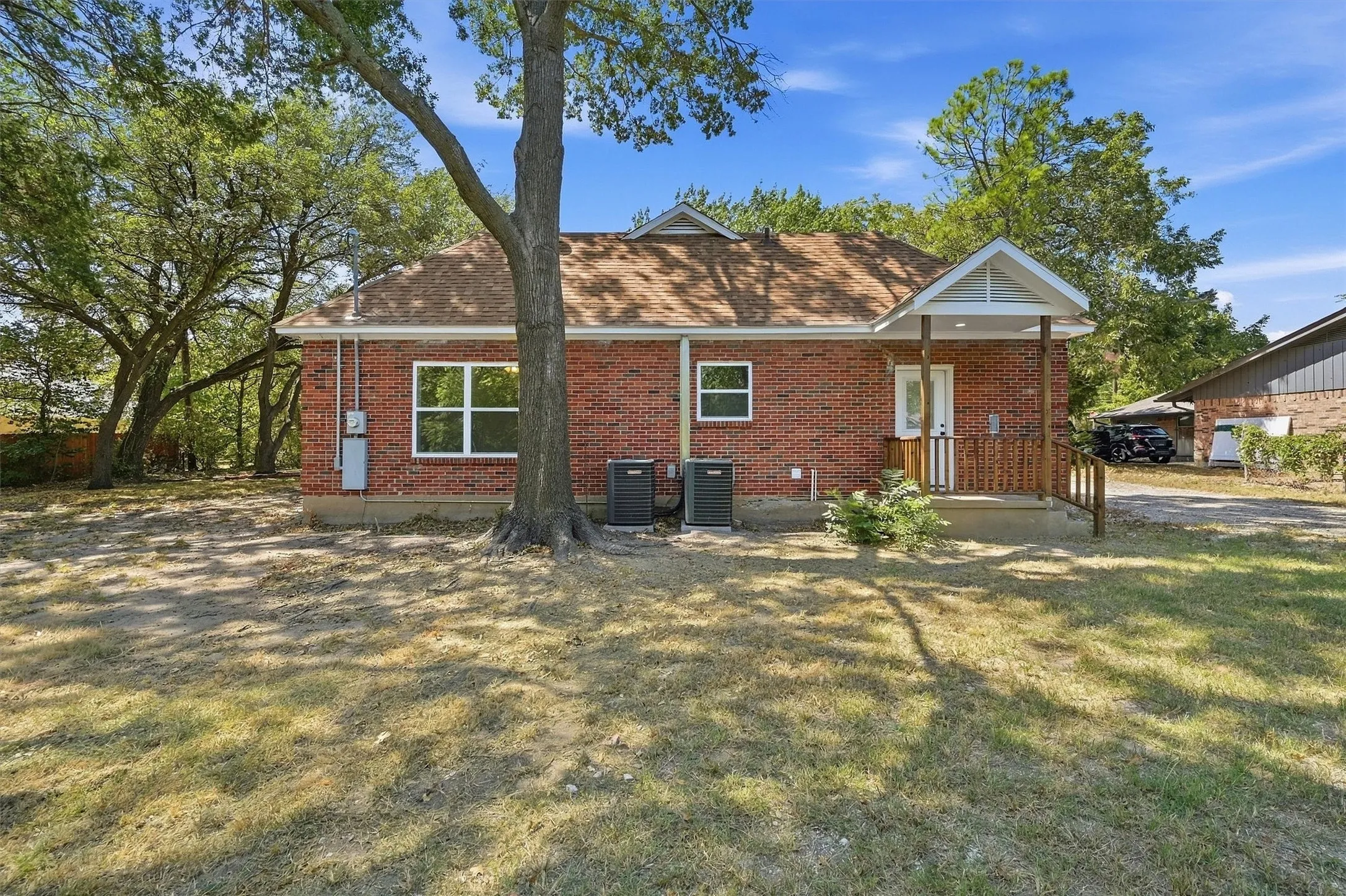 Brick exterior with white frame windows, covered porch with wood railings, and mature trees providing shade