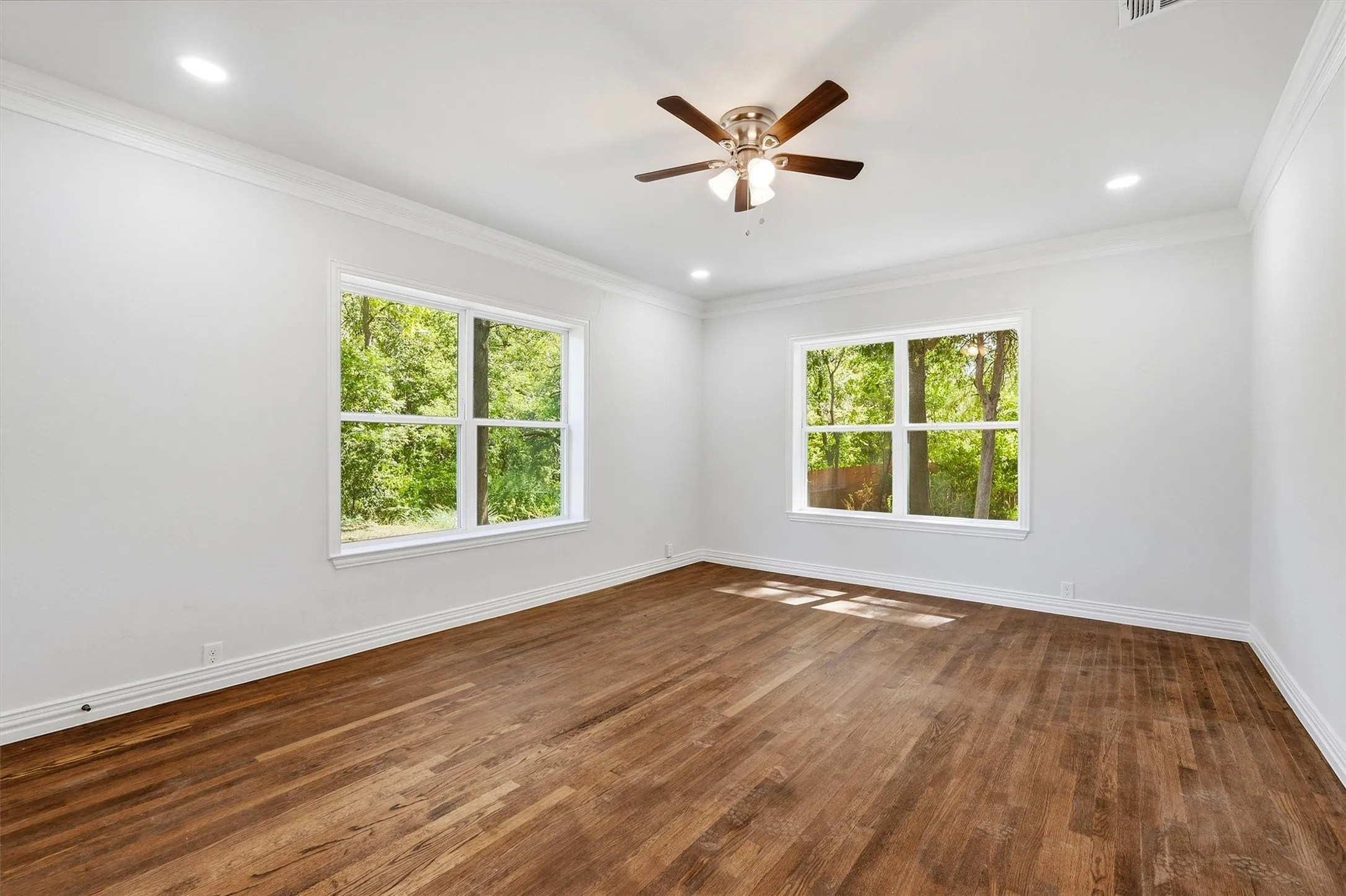 Bright interior featuring wood-finish flooring, two large windows, a ceiling fan, recessed lighting, and crown molding