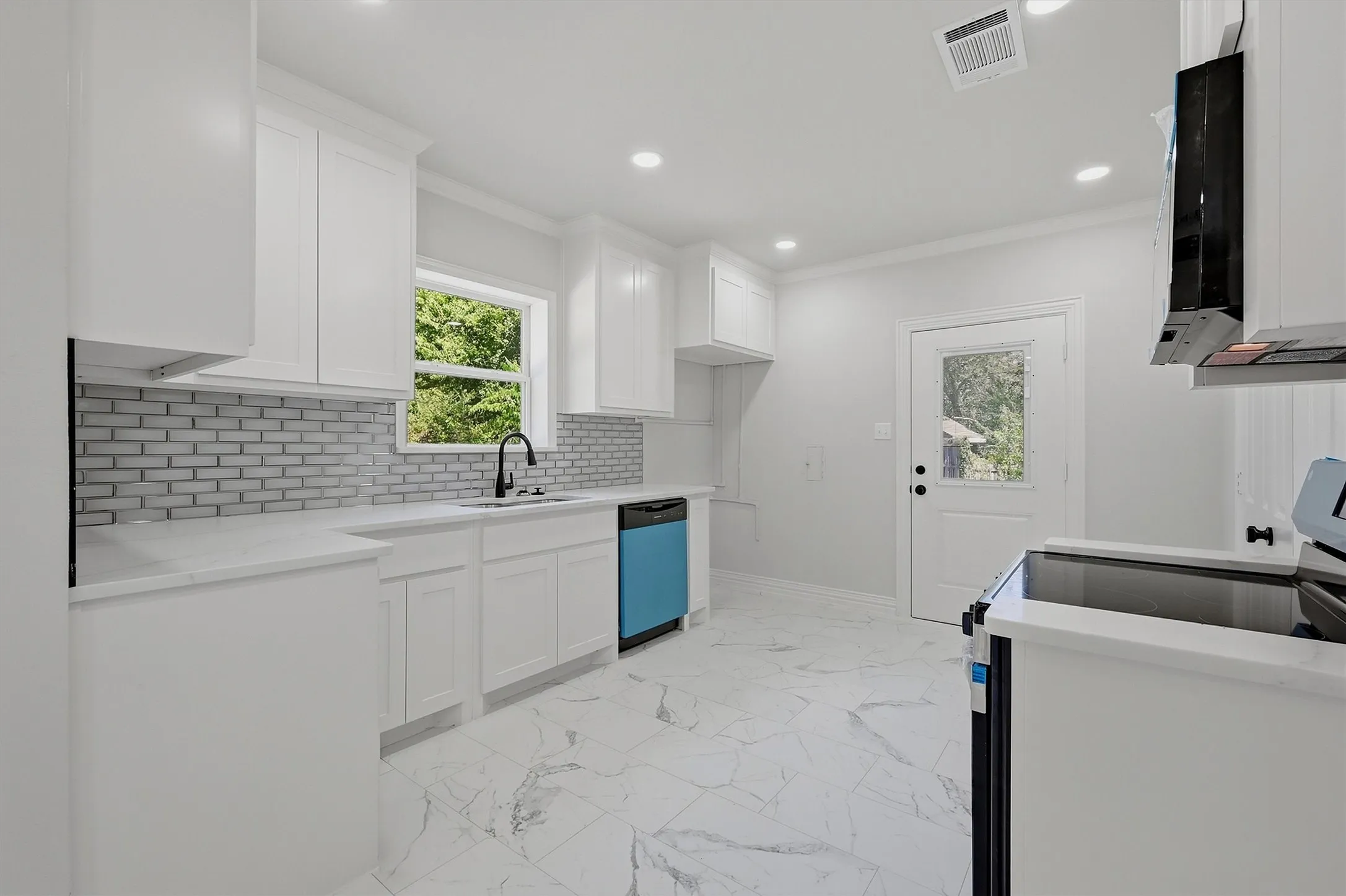 Kitchen featuring white shaker cabinetry, light-toned countertops, subway tile backsplash, recessed lighting, and a single-light door