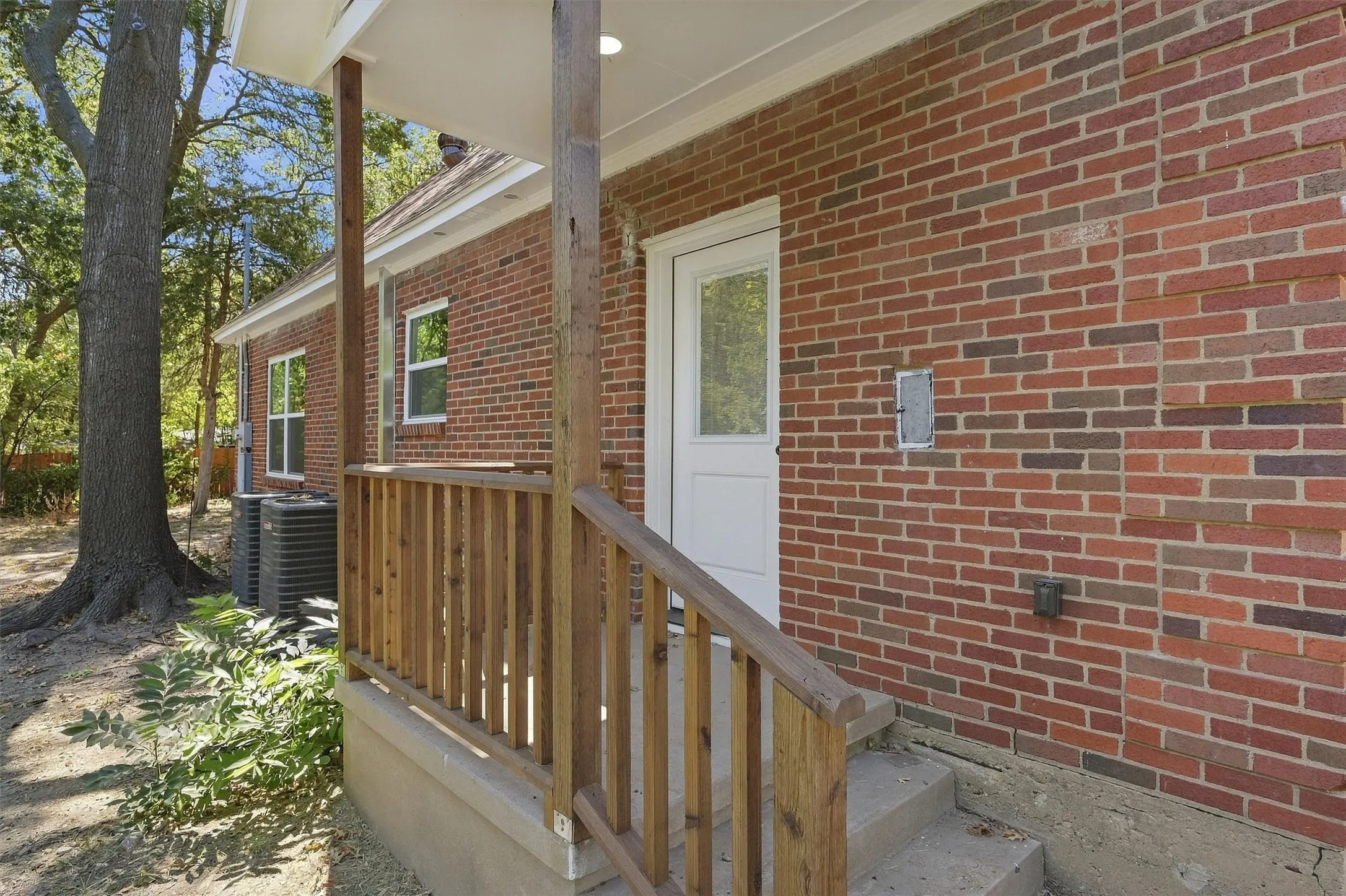Brick exterior with multiple windows, wooden porch railing, and a white entry door