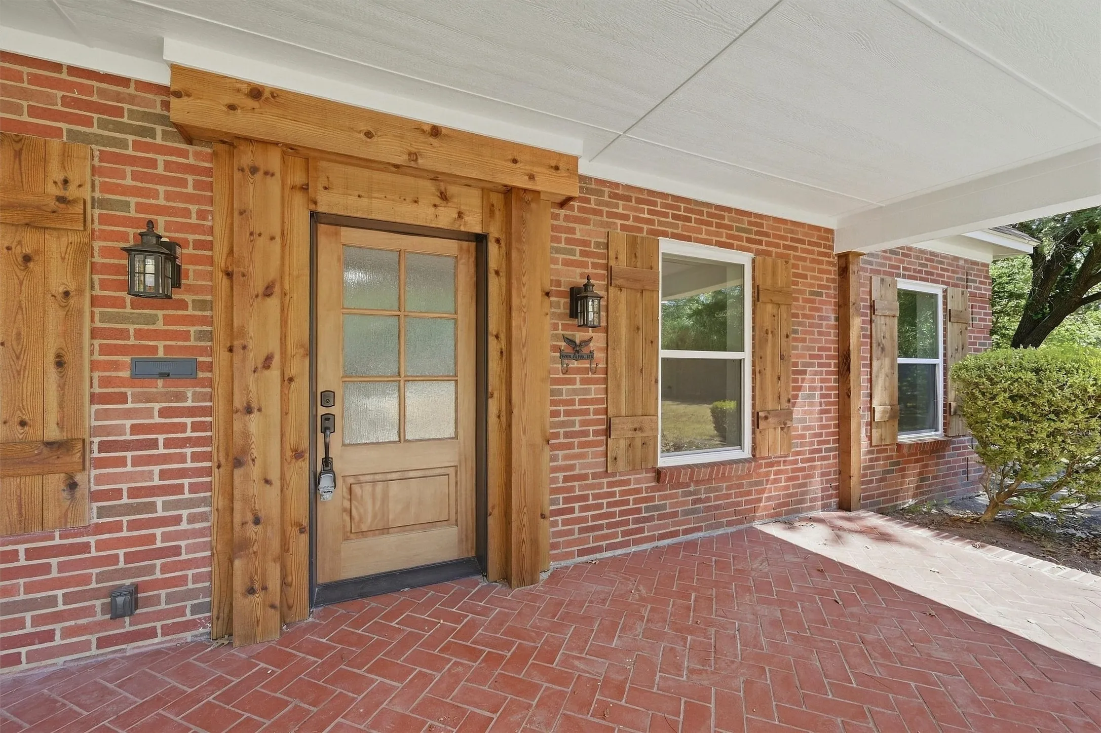 Brick exterior featuring a wood-panel entry door, decorative wood shutters, and herringbone-patterned brick flooring