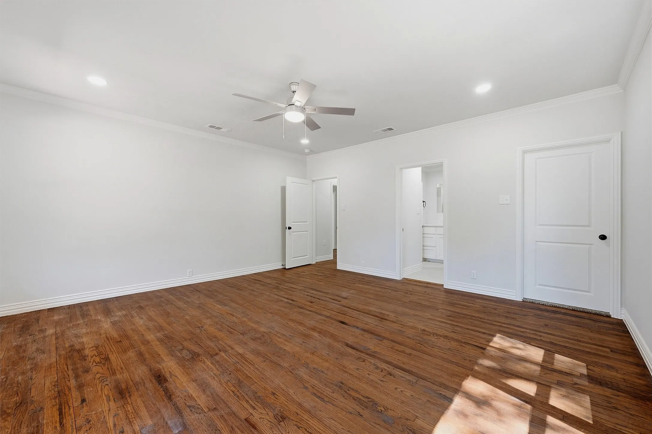 Wood-finish flooring with crisp white walls, crown molding, and recessed lighting