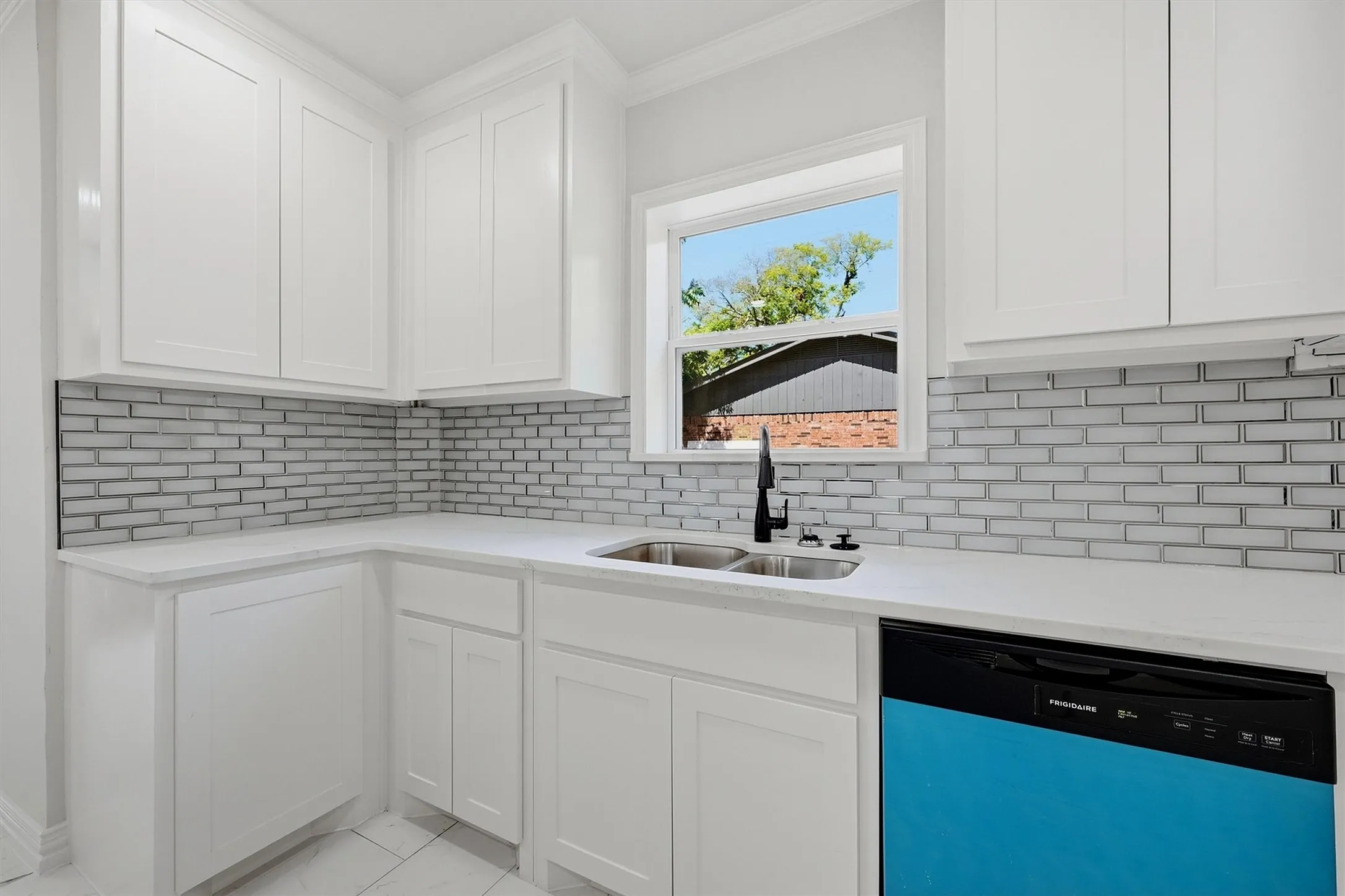 White shaker-style cabinetry, white countertops, subway tile backsplash, stainless steel double-basin sink, and a black faucet