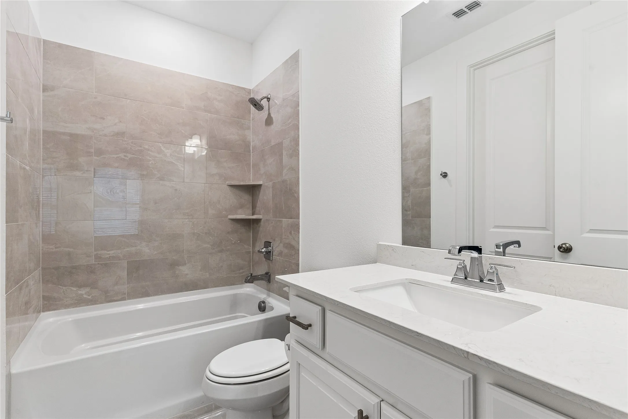 Shower/tub combination with tile surround, white vanity with integrated sink, chrome fixtures, and white cabinetry