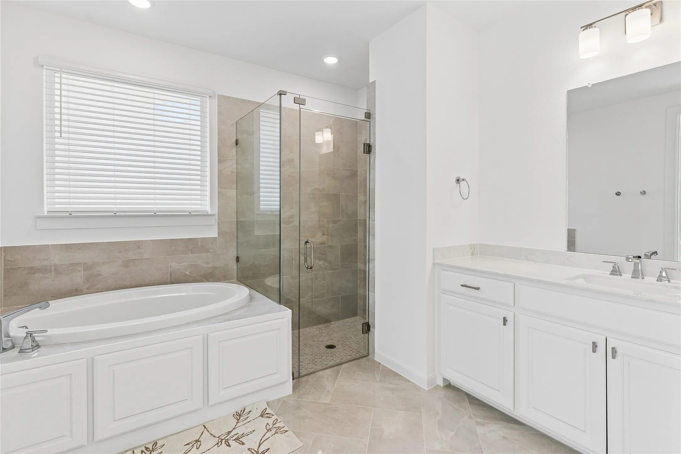 Soaking tub with white cabinetry, glass-enclosed shower, dual vanity with undermount sinks, and tile flooring