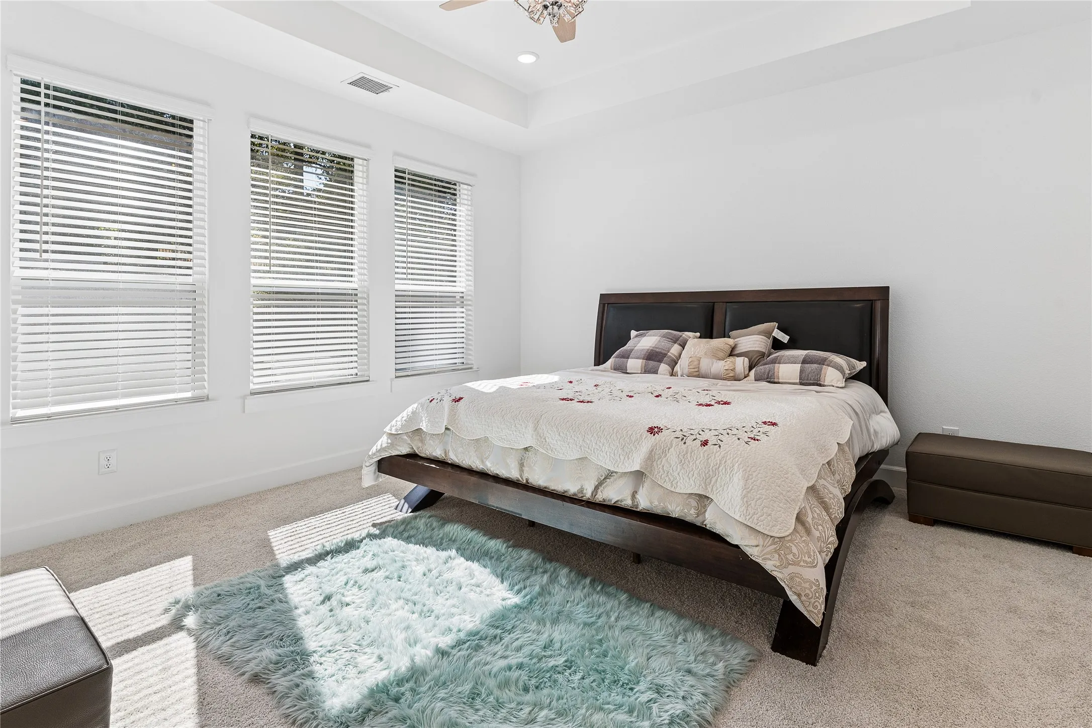 Tray ceiling with recessed lighting, ceiling fan, three windows with blinds, and carpeted flooring