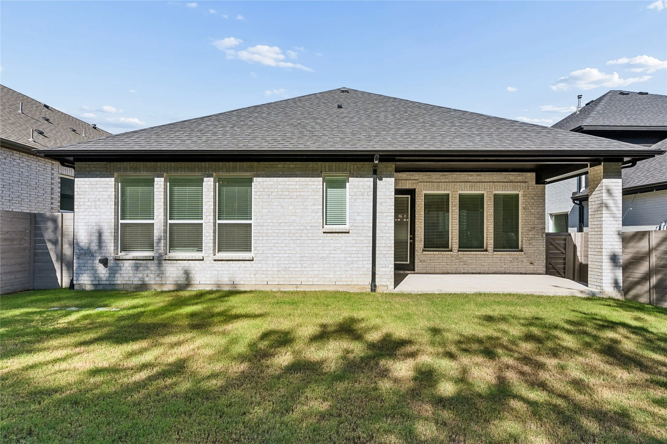 Exterior featuring light brick construction, a covered patio, a dark shingle roof, and multiple windows