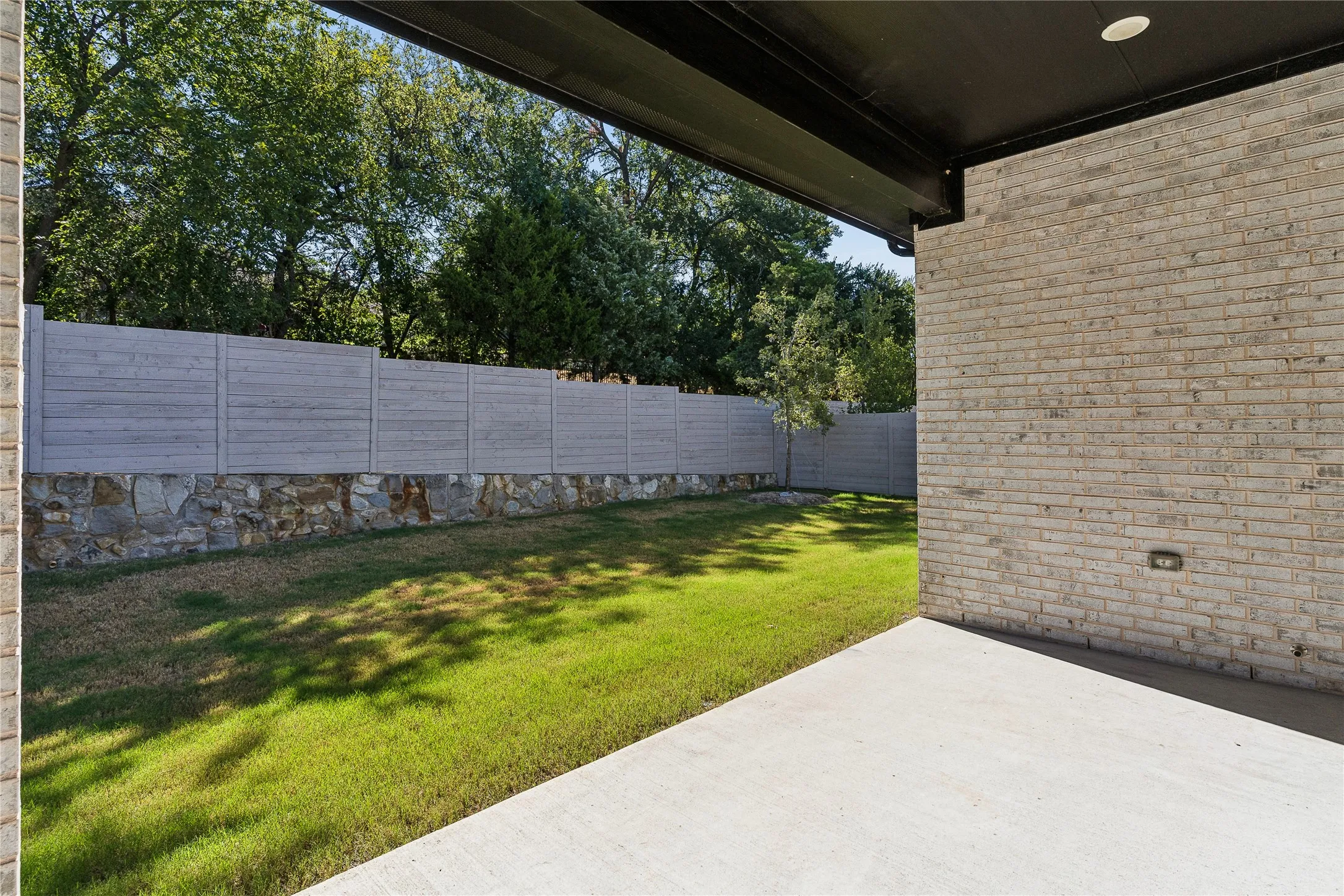 Concrete patio with a light-colored brick exterior wall, black overhang, and recessed lighting