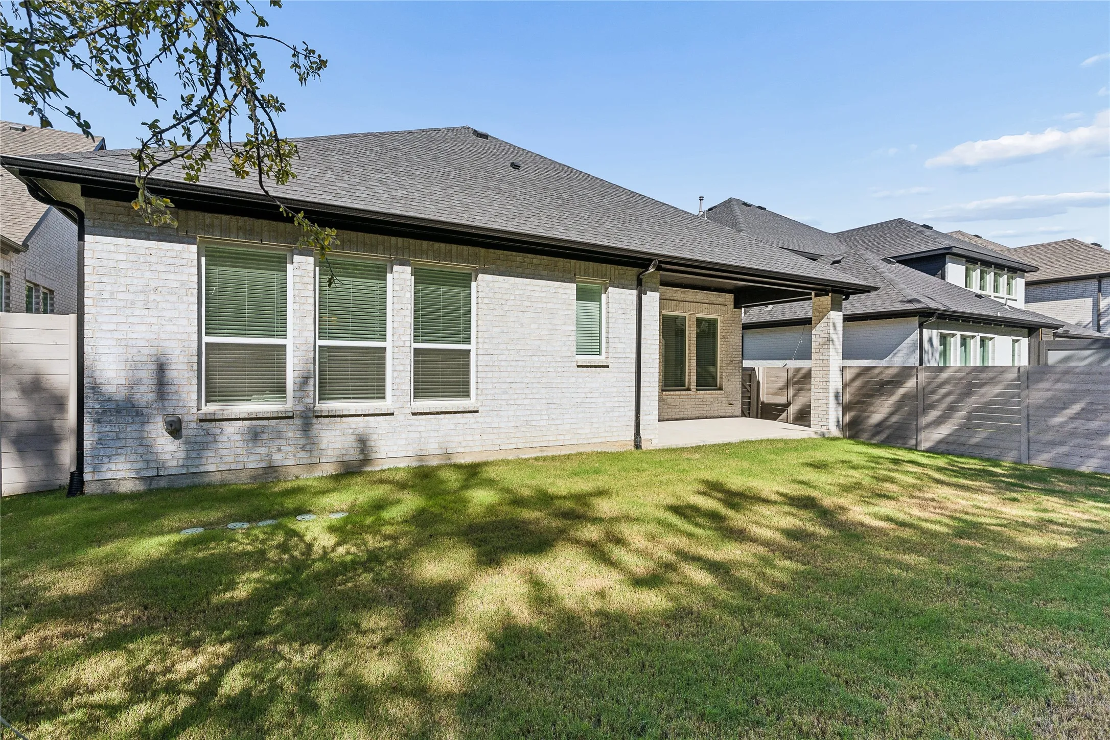 White brick exterior with a covered patio, dark shingle roof, and a privacy fence