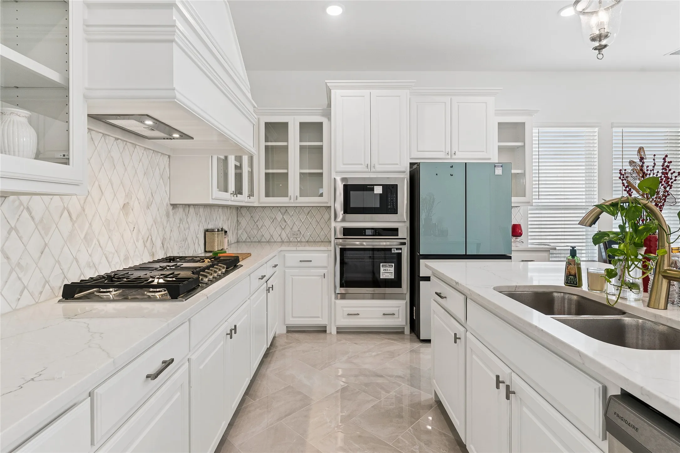 White cabinetry with glass-front accents, stainless steel built-in appliances, a gas cooktop, and a double basin sink