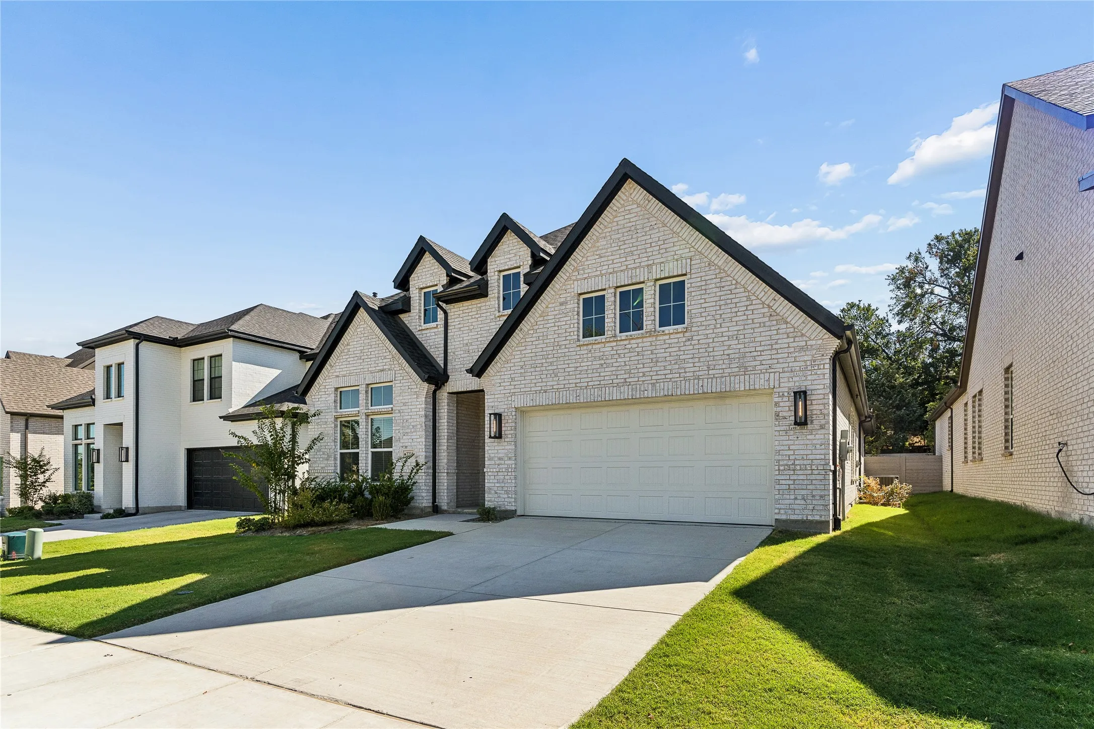 White brick exterior with black trim, a gabled roofline, an attached two-car garage, and a concrete driveway