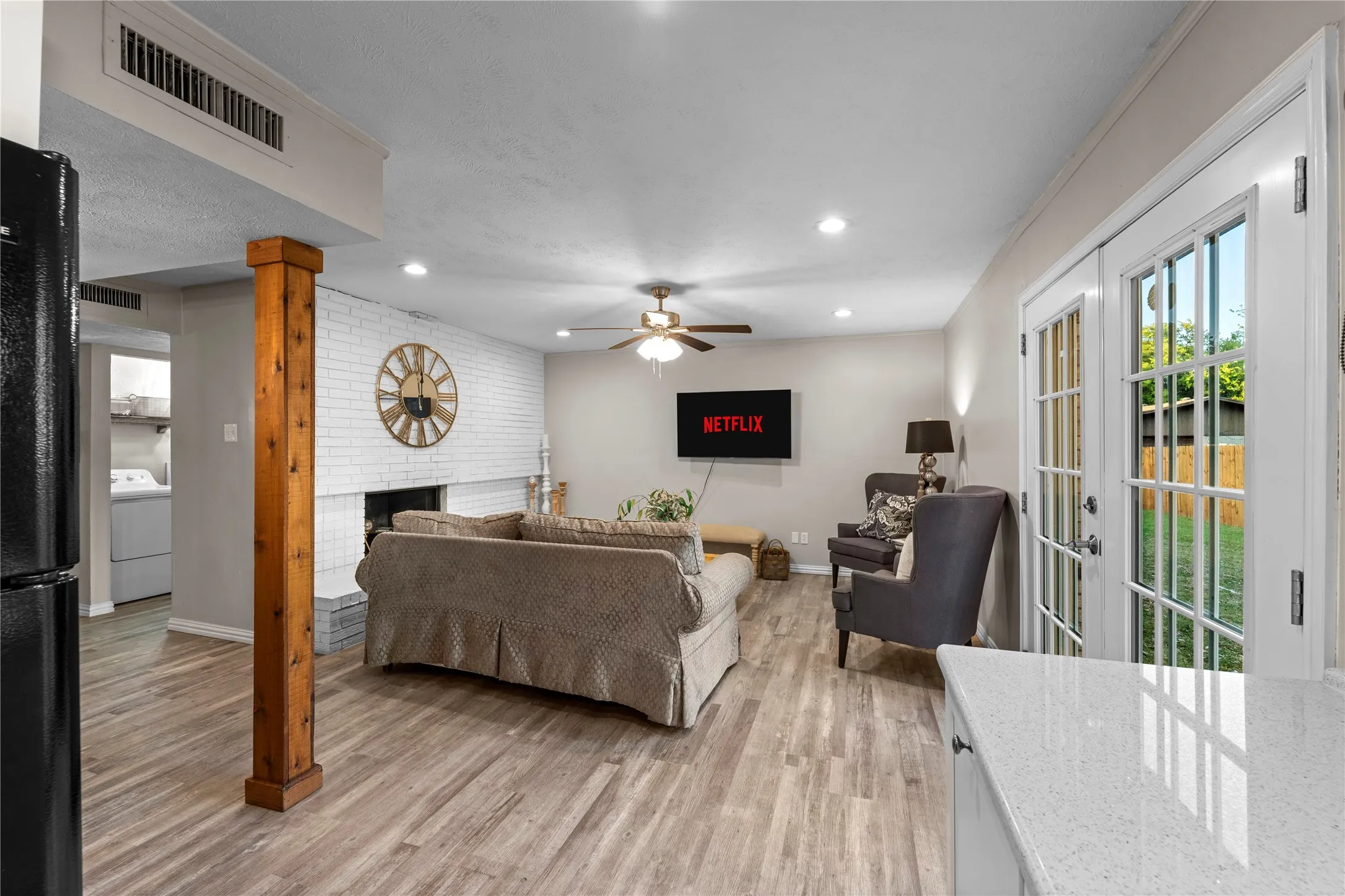 Wood-finish flooring throughout, white painted brick fireplace, recessed lighting, ceiling fan, and double glass-paneled doors