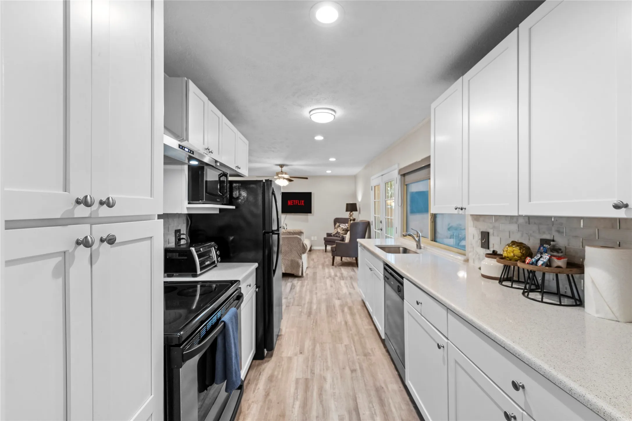 Galley kitchen featuring white cabinetry, light-toned countertops, a stainless steel sink, and wood-finish flooring