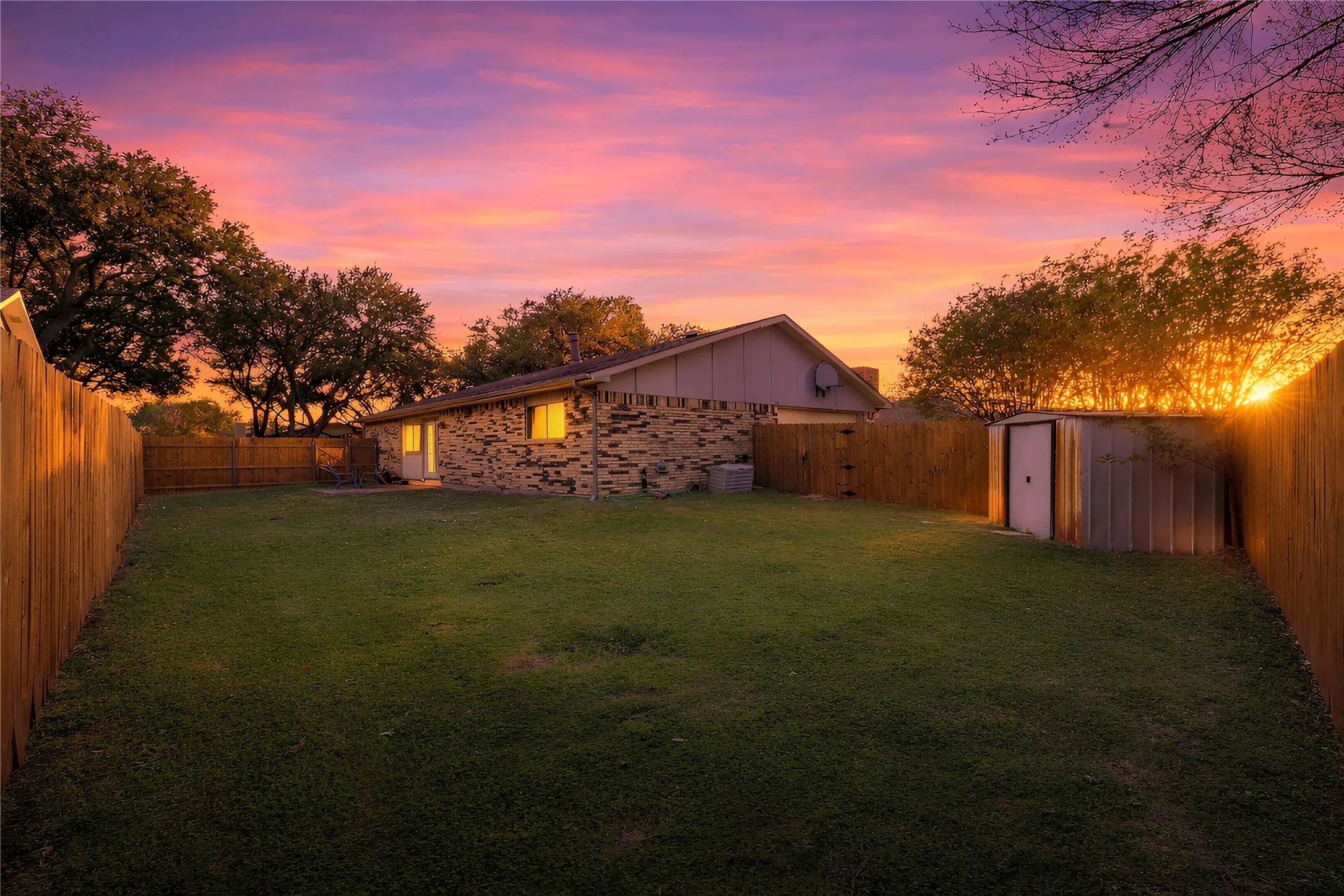 Expansive backyard featuring a manicured lawn, full privacy fencing, and a detached storage shed