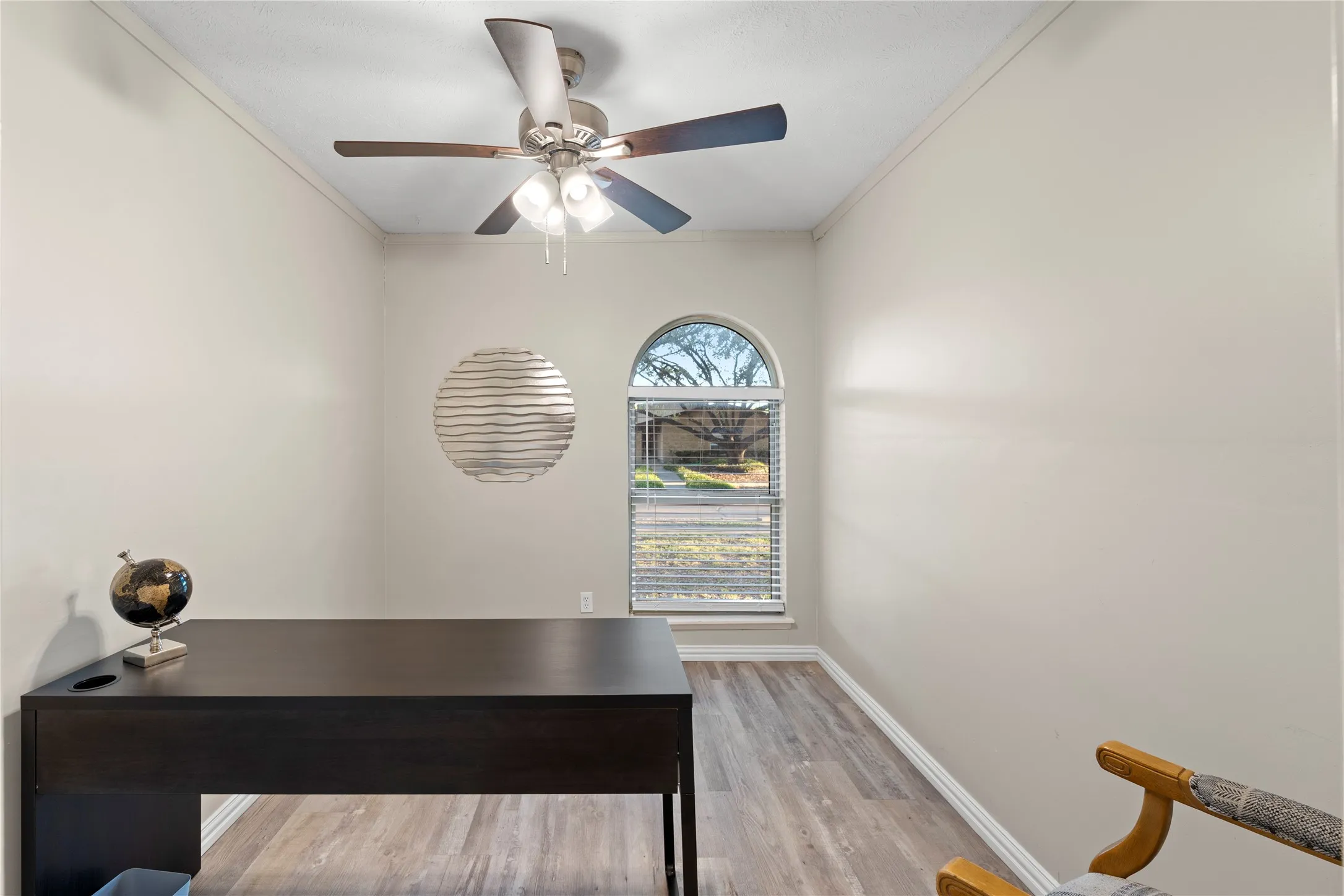 Arched window with blinds, wood-finish flooring, and ceiling fan