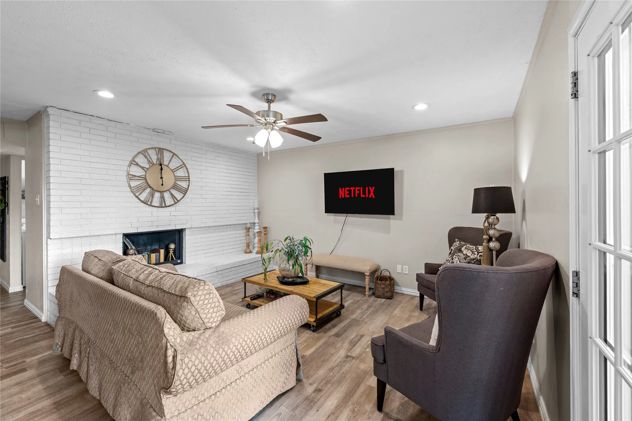 Living area featuring wood-finish flooring, a white brick fireplace, recessed lighting, and a ceiling fan