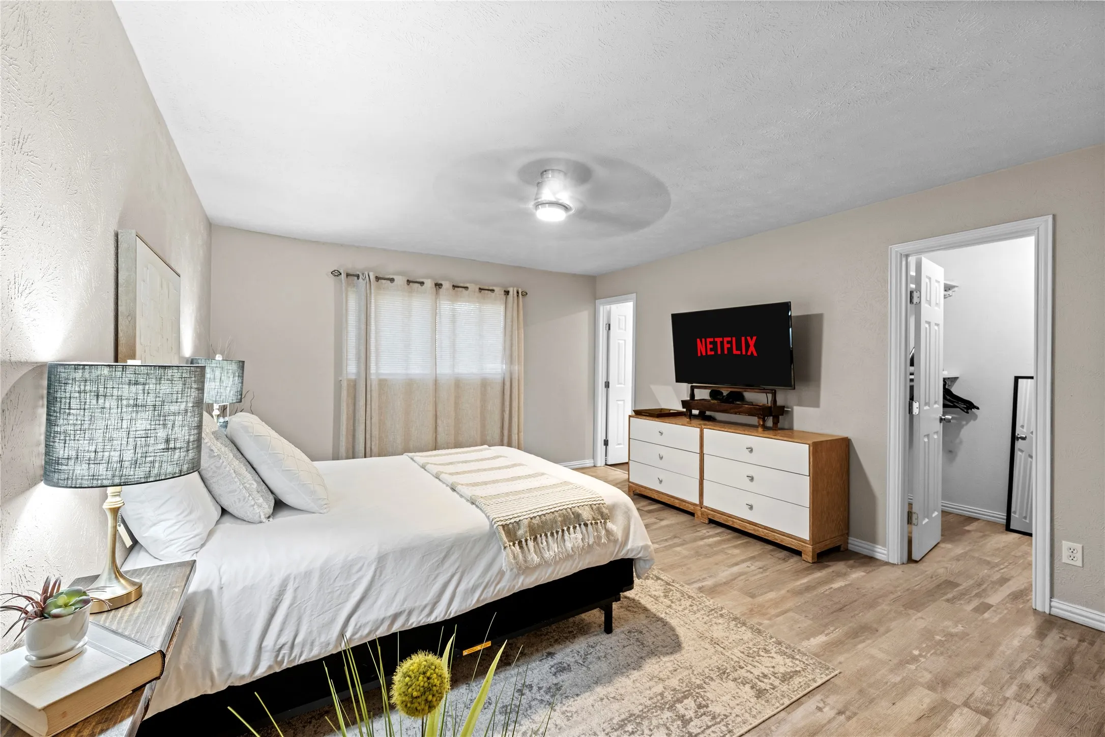 Wood-finish flooring, ceiling fan, and window with sheer curtains