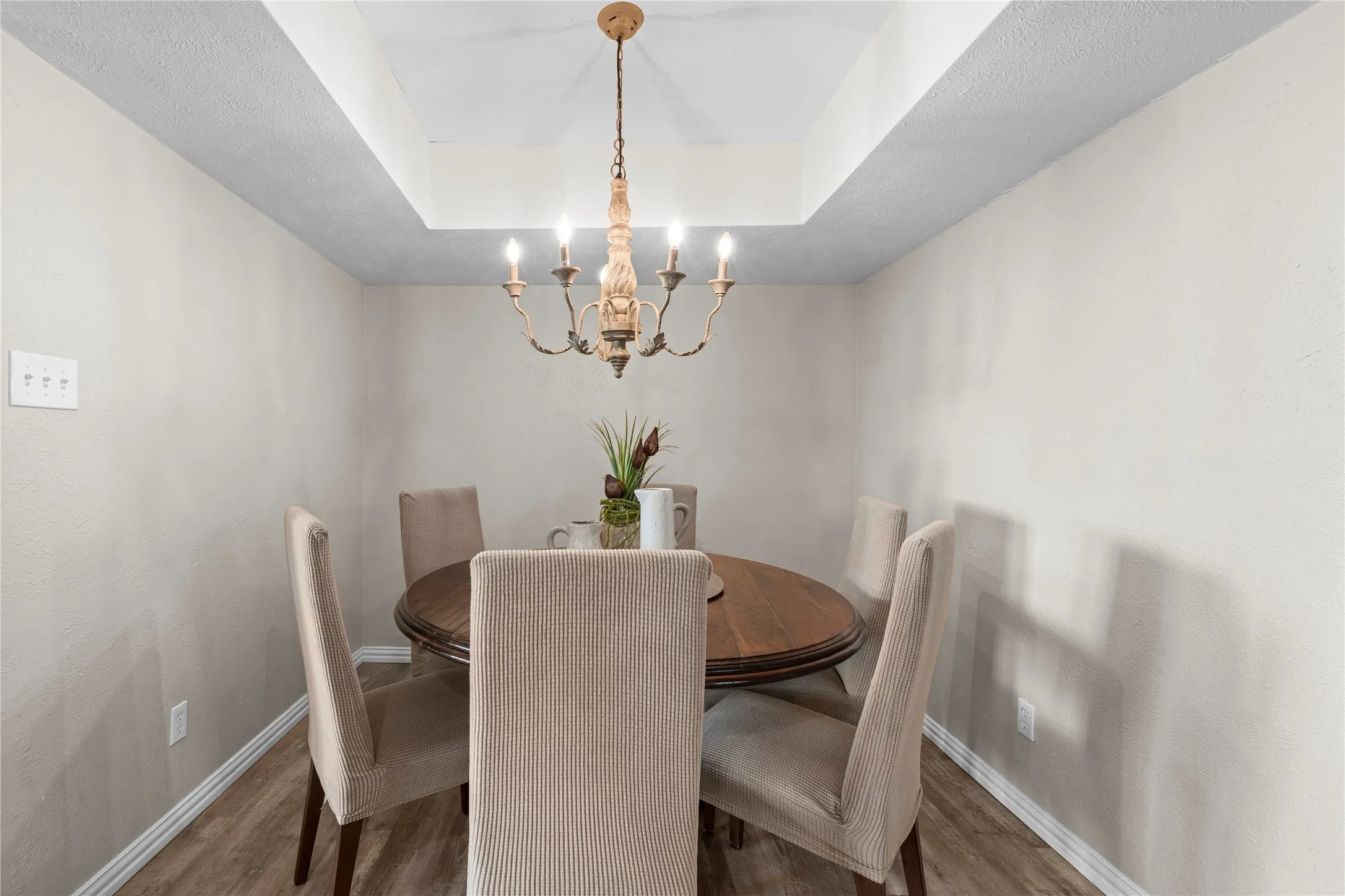 Tray ceiling with a decorative chandelier, wood-finish flooring, and neutral wall tones
