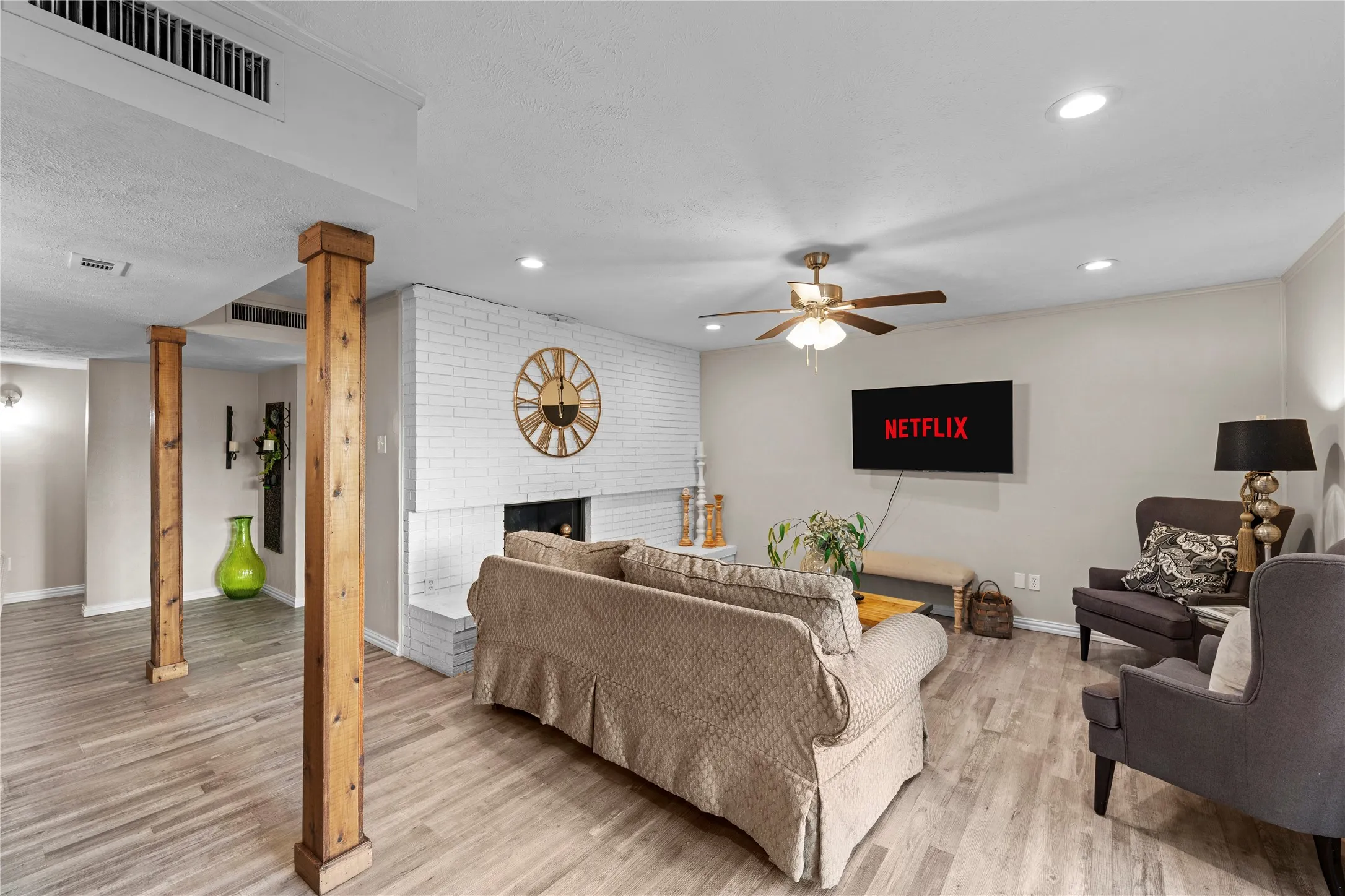 Spacious living area featuring wood-finish flooring, recessed lighting, and a white brick fireplace