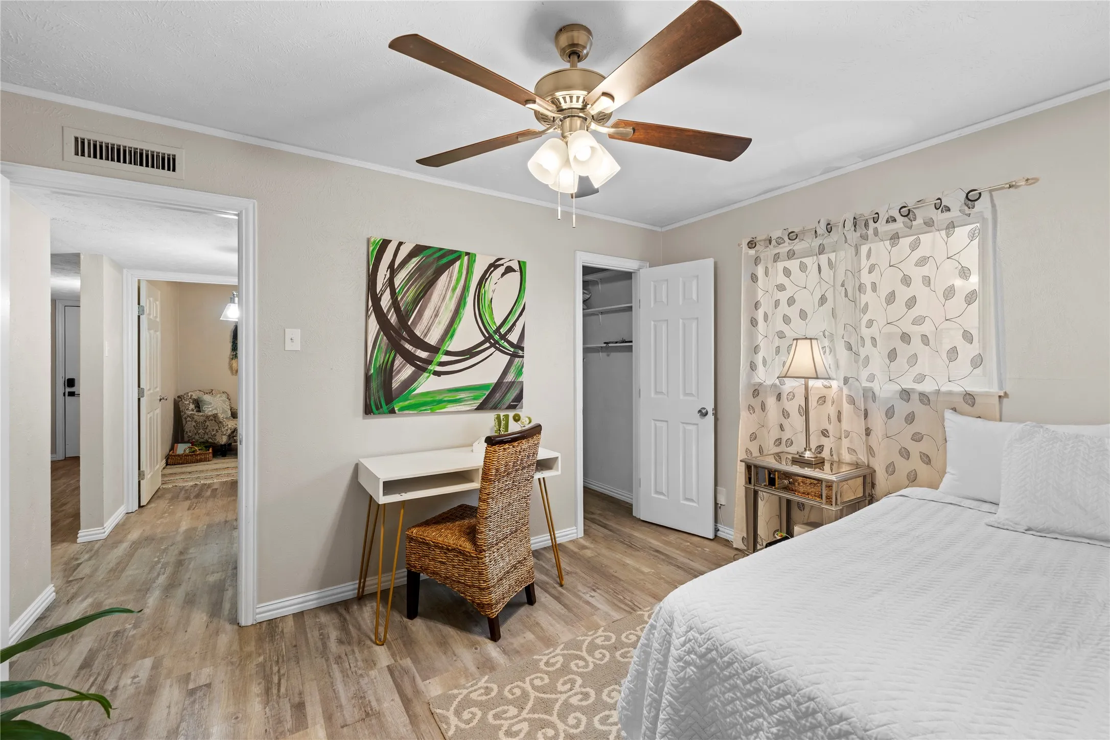 Wood-finish flooring throughout, ceiling fan with integrated lighting, window with light-filtering curtains, and a built-in closet with shelving