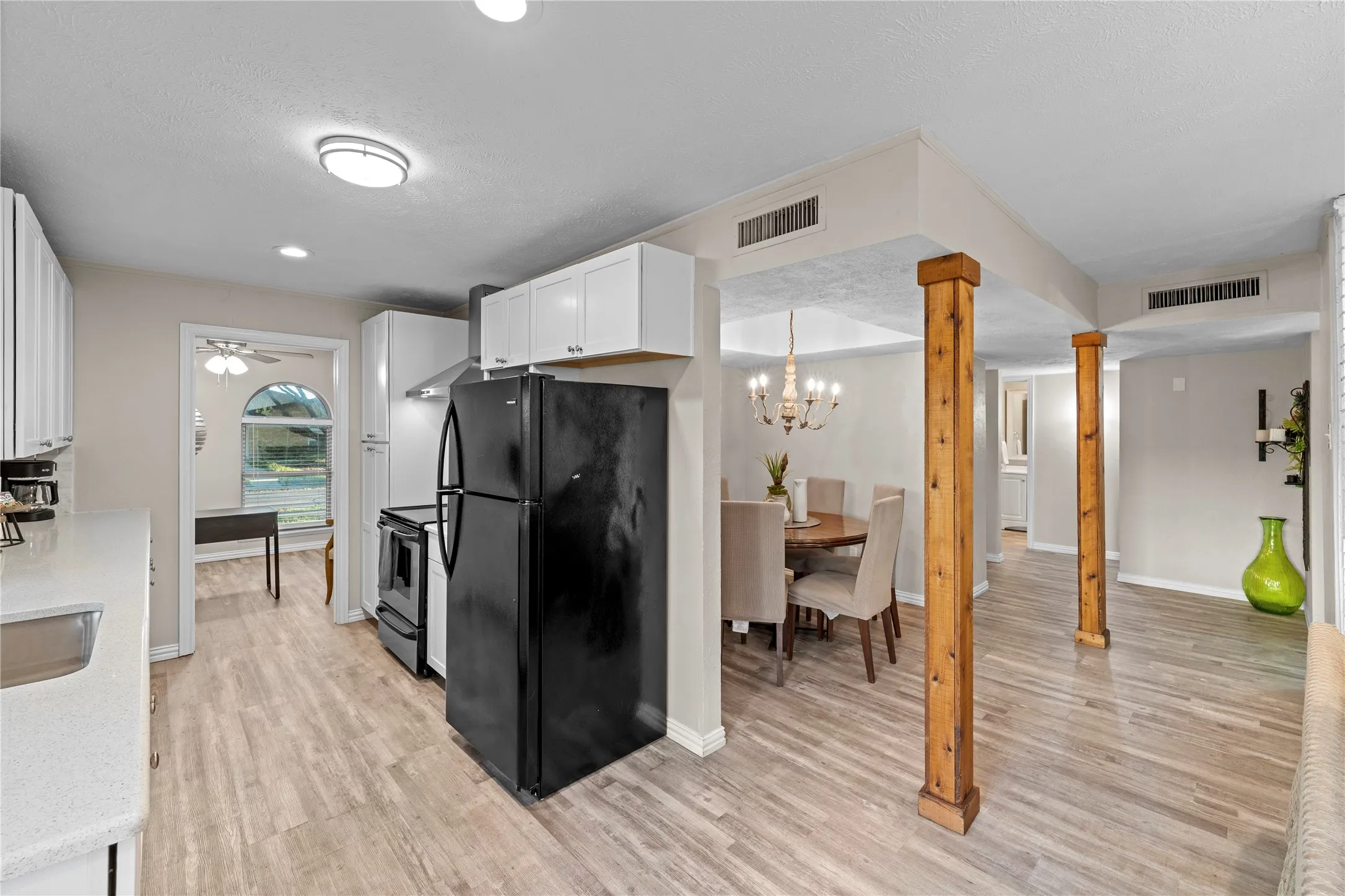Kitchen with white cabinetry, stainless steel range hood, black appliances, and light wood-finish flooring