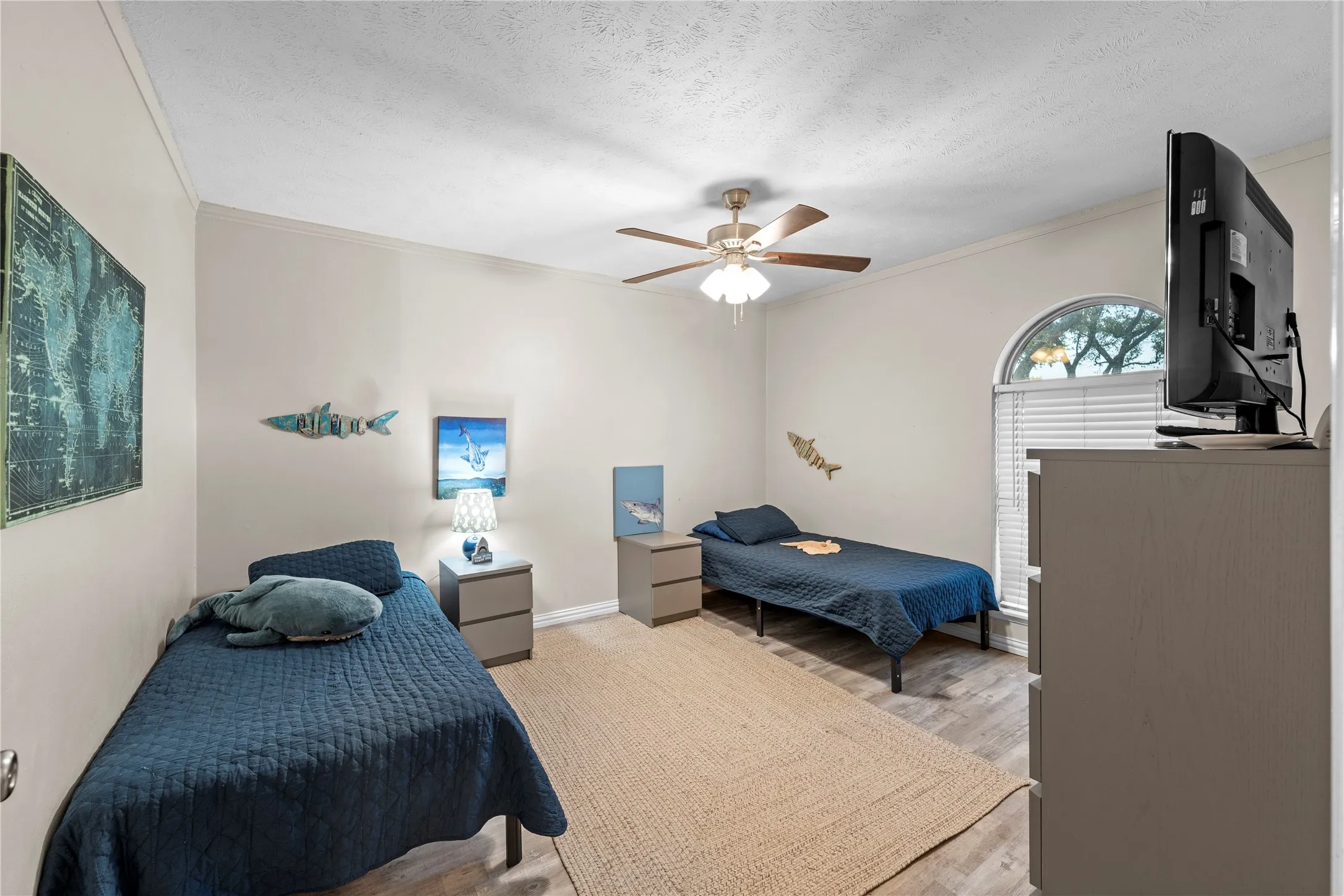 Neutral wall finishes, wood-finish flooring, ceiling fan with integrated lighting, arched window with horizontal blinds, built-in storage unit