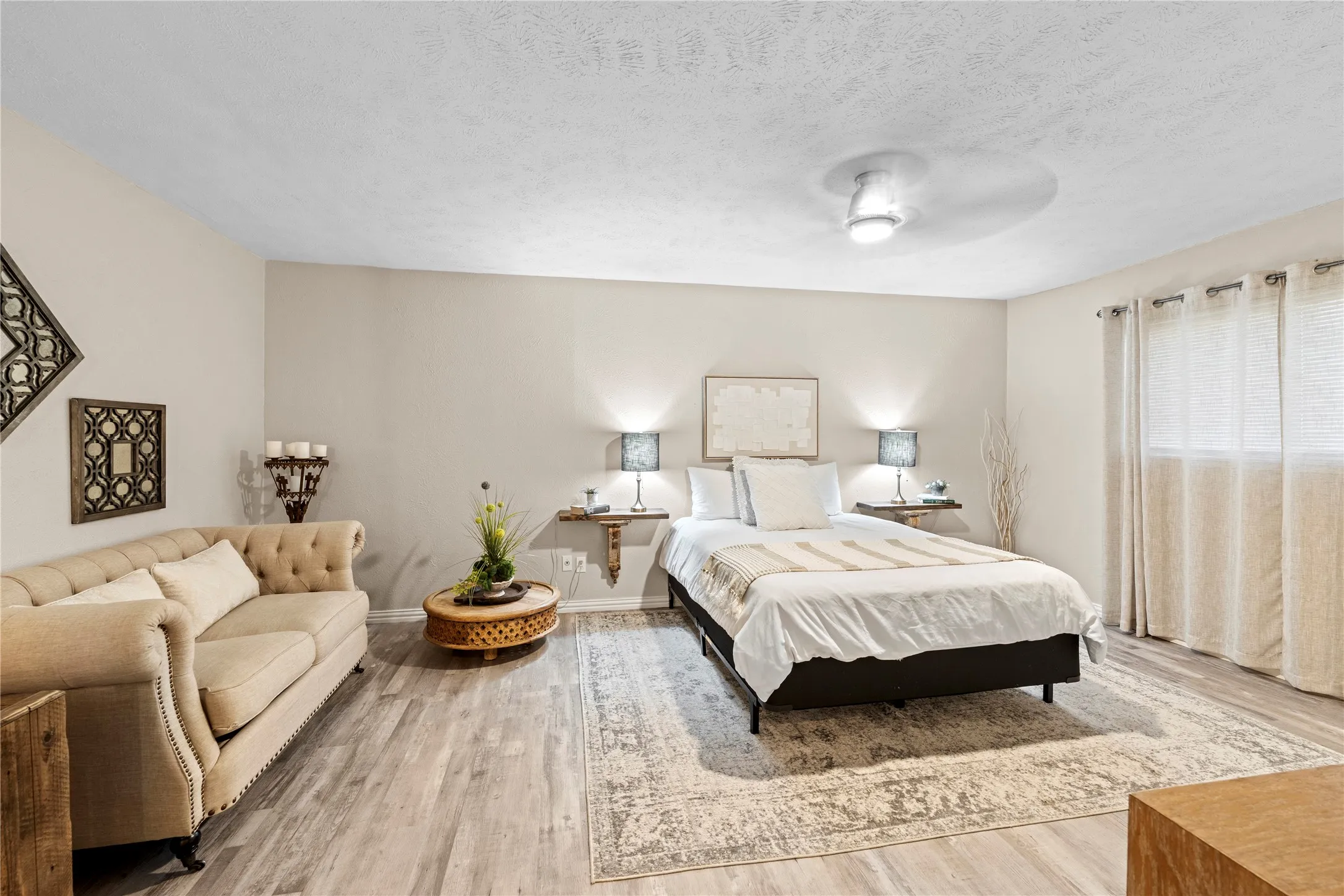 Light-toned wood-finish flooring, neutral wall color, recessed ceiling light with fan, and window with light-filtering drapes
