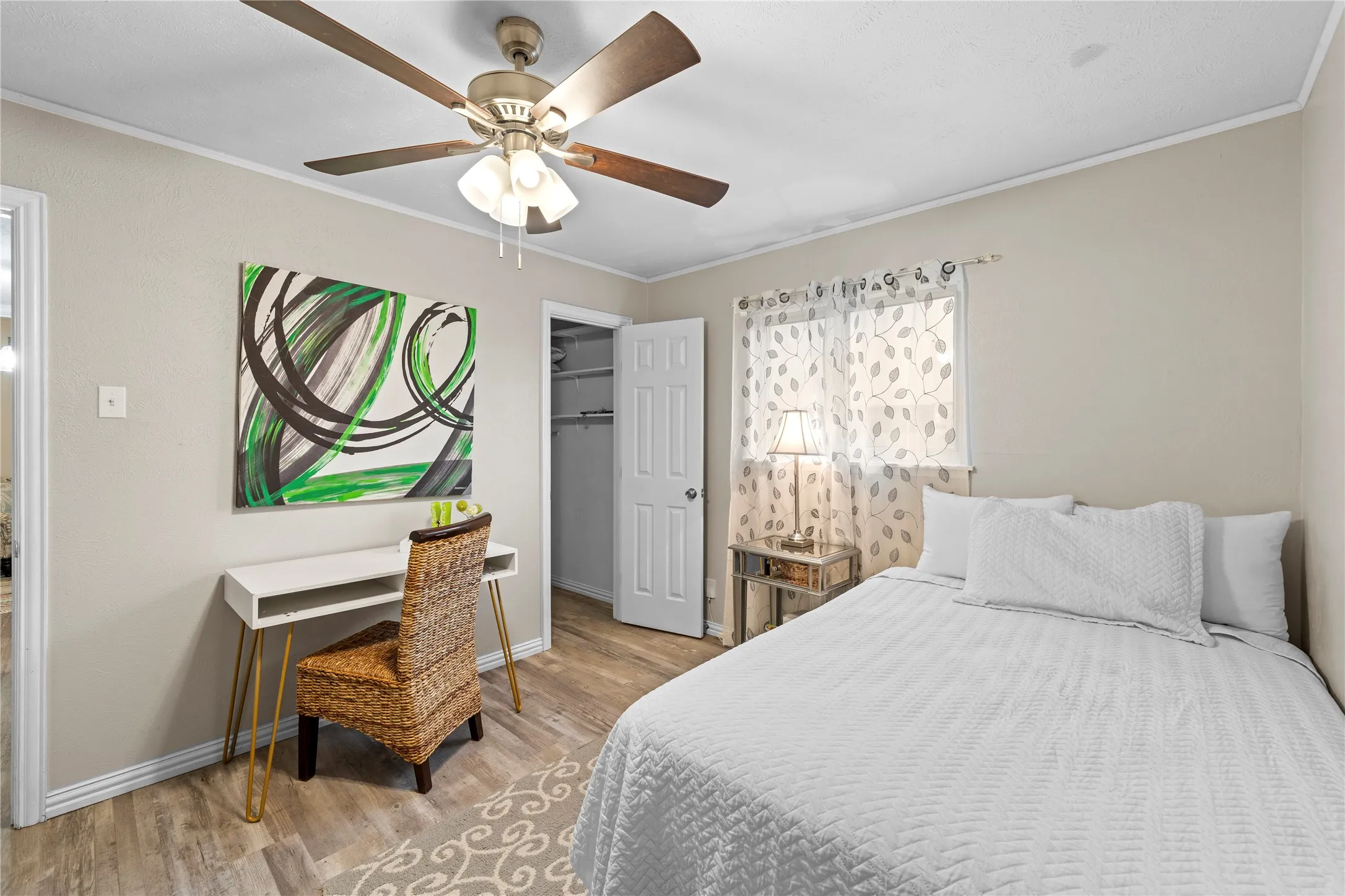 Wood-finish flooring, ceiling fan with integrated lighting, window with sheer treatments, and an open closet