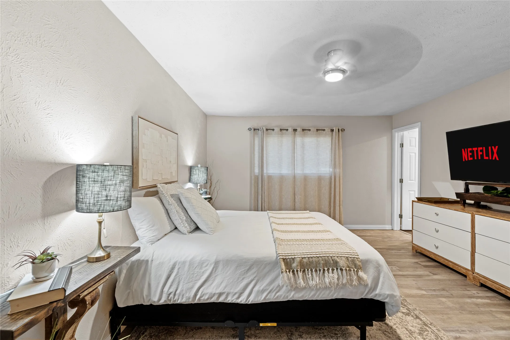 Wood-finish flooring, ceiling fan with integrated lighting, window with drapes, and a built-in closet with a white panel door