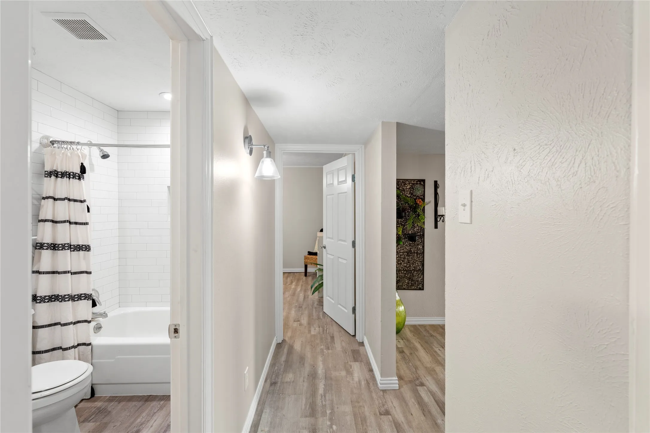 Bathroom featuring a white bathtub with subway tile surround, chrome shower fixtures, and wood-finish flooring