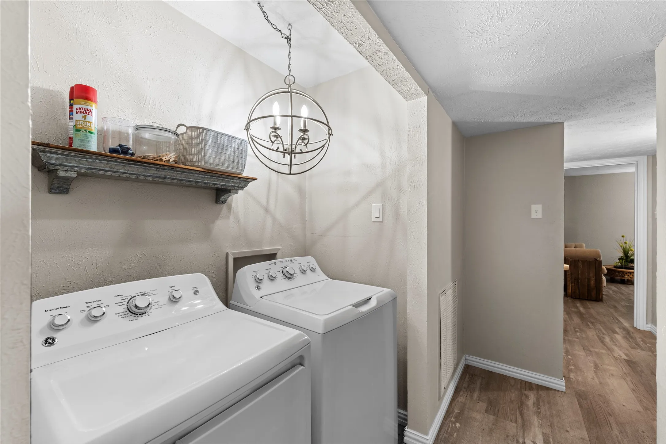 Laundry area featuring a decorative orb light fixture, wall-mounted shelving, and wood-finish flooring