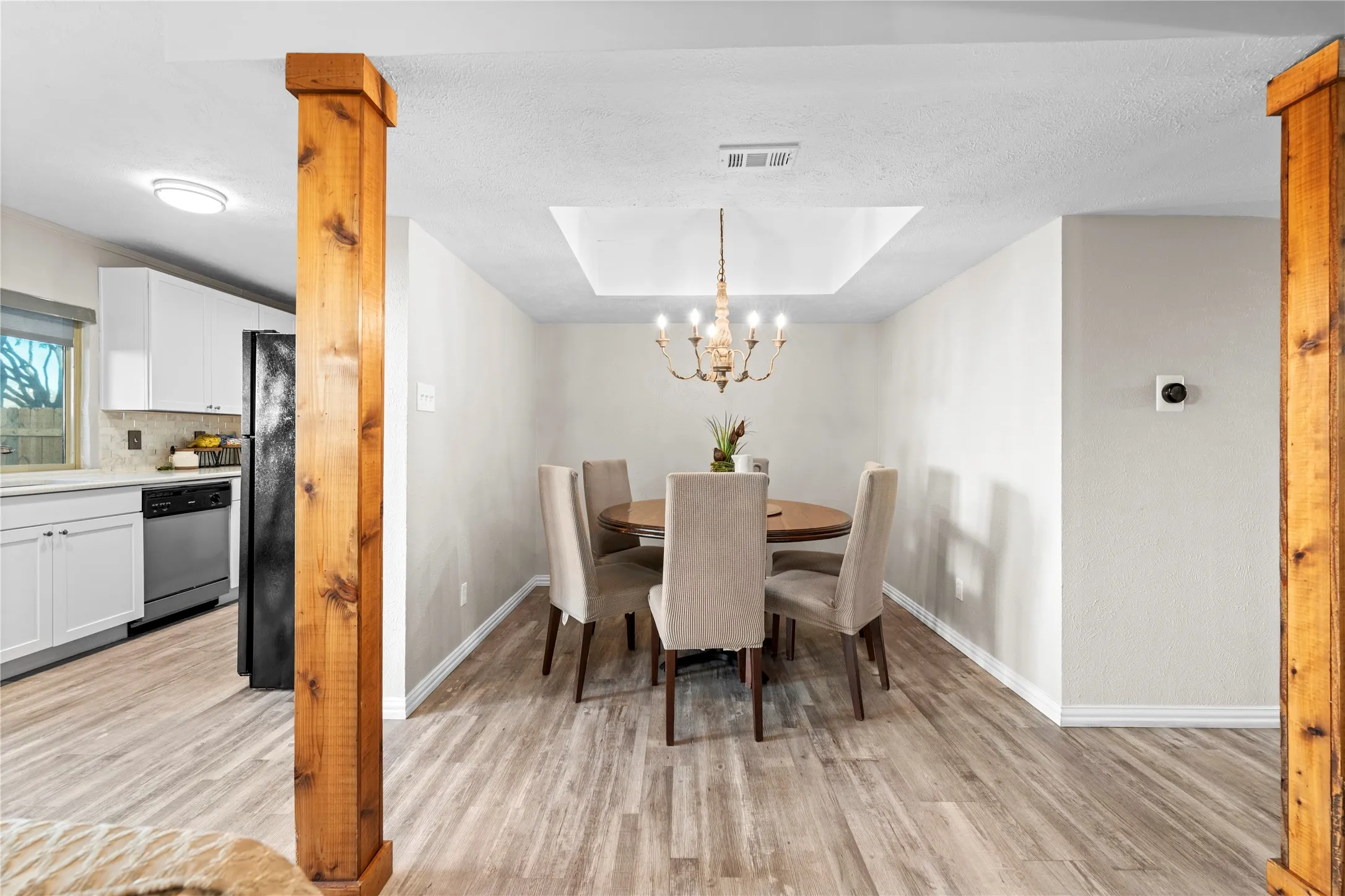 Dining area with wood-finish flooring, a recessed ceiling feature, and a chandelier