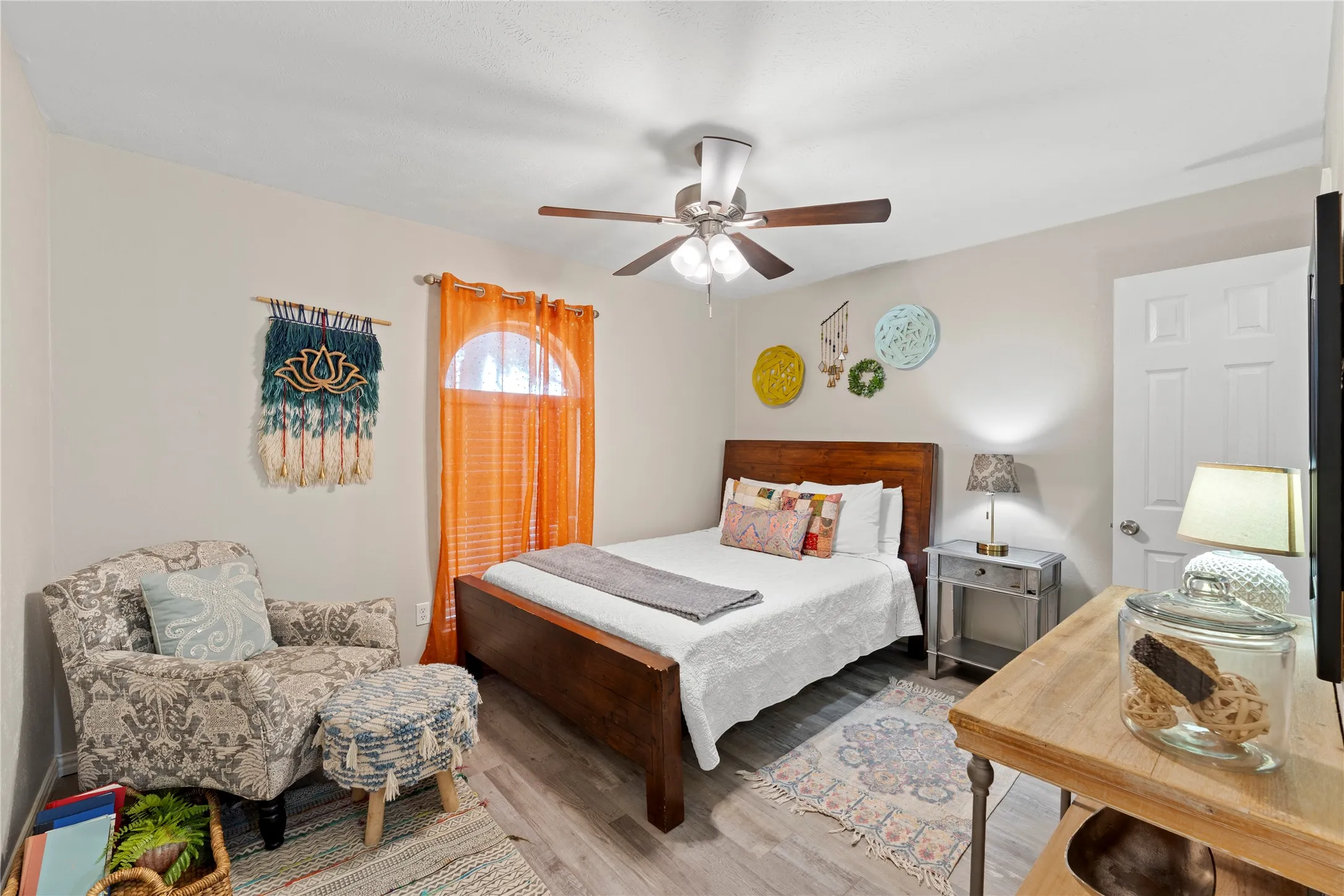 Light gray wall paint, wood-finish flooring, ceiling fan with integrated lighting, arched window, paneled door