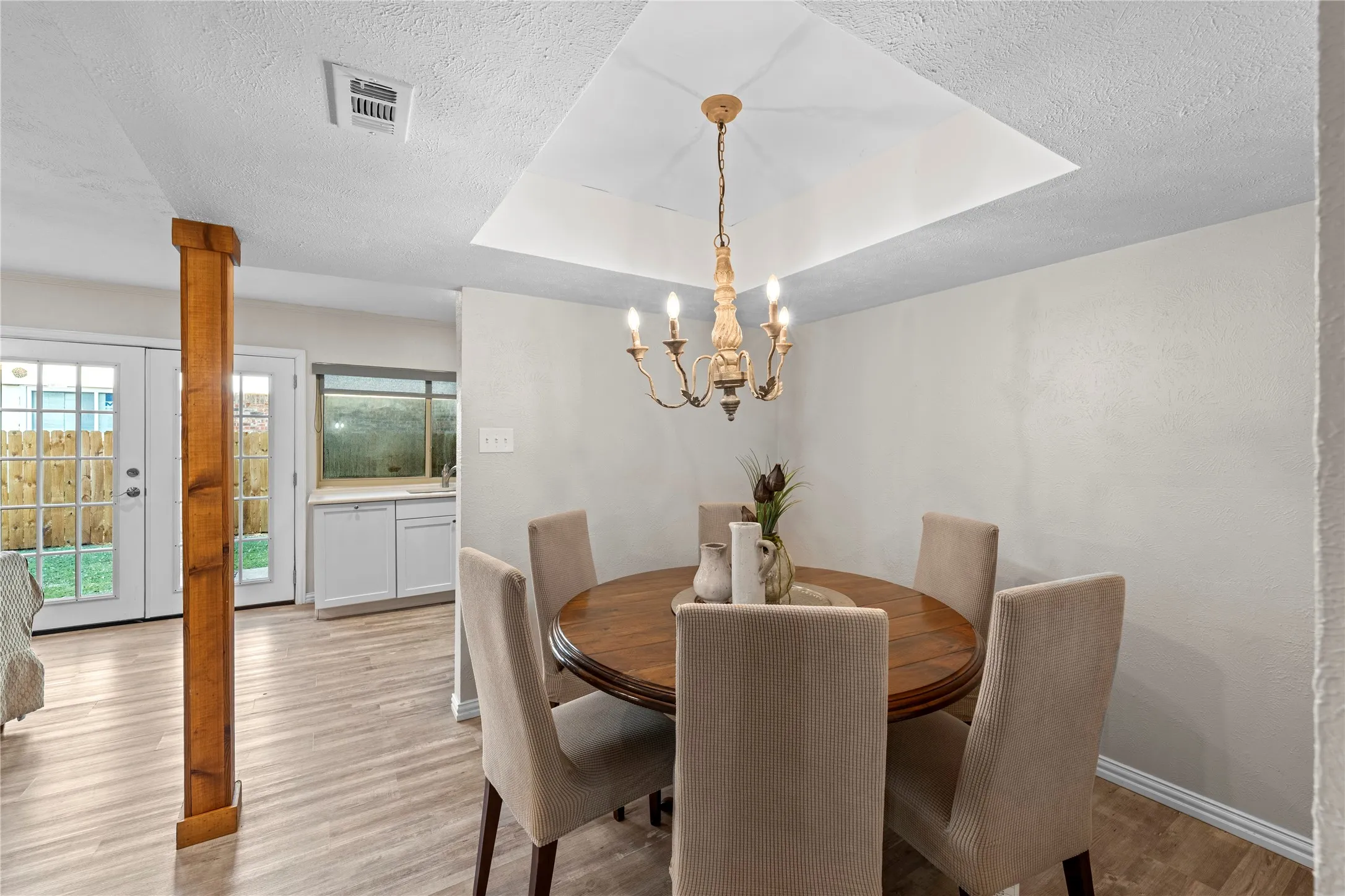 Tray ceiling with chandelier, light wood-finish flooring, and white walls
