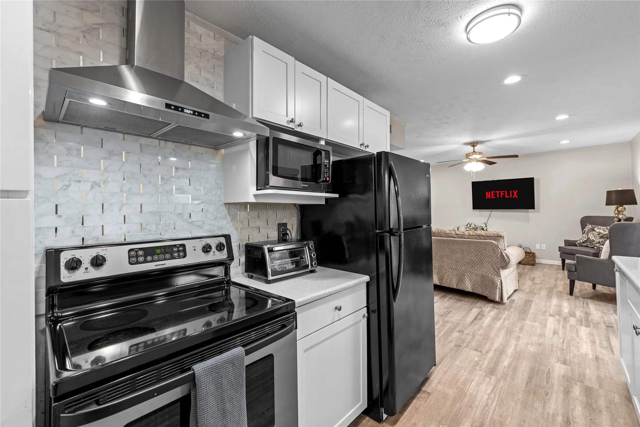 Kitchen featuring stainless steel range hood, white shaker cabinetry, and a light-toned backsplash
