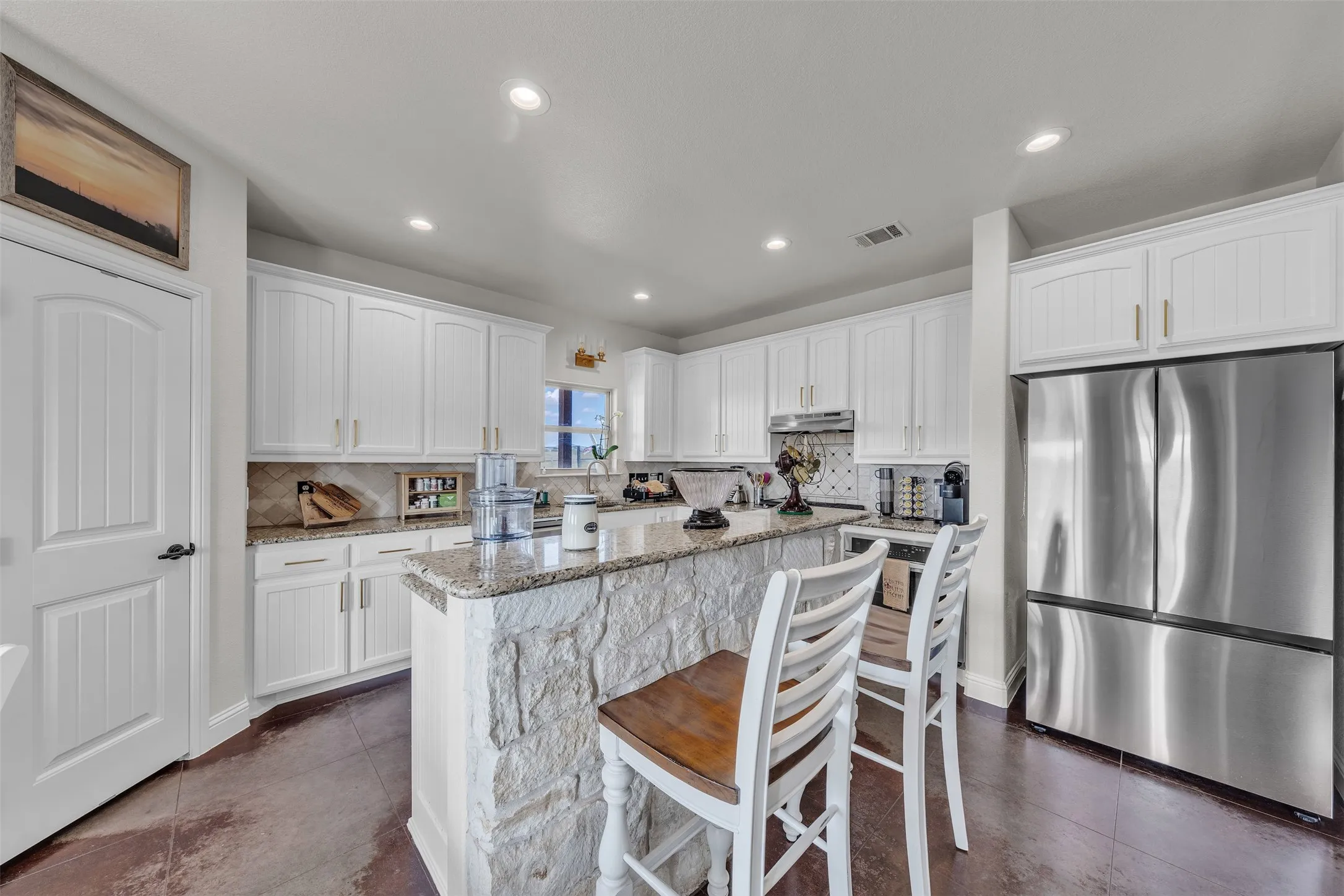 Kitchen featuring white cabinetry, stone-clad island with granite countertops, stainless steel refrigerator, and recessed lighting