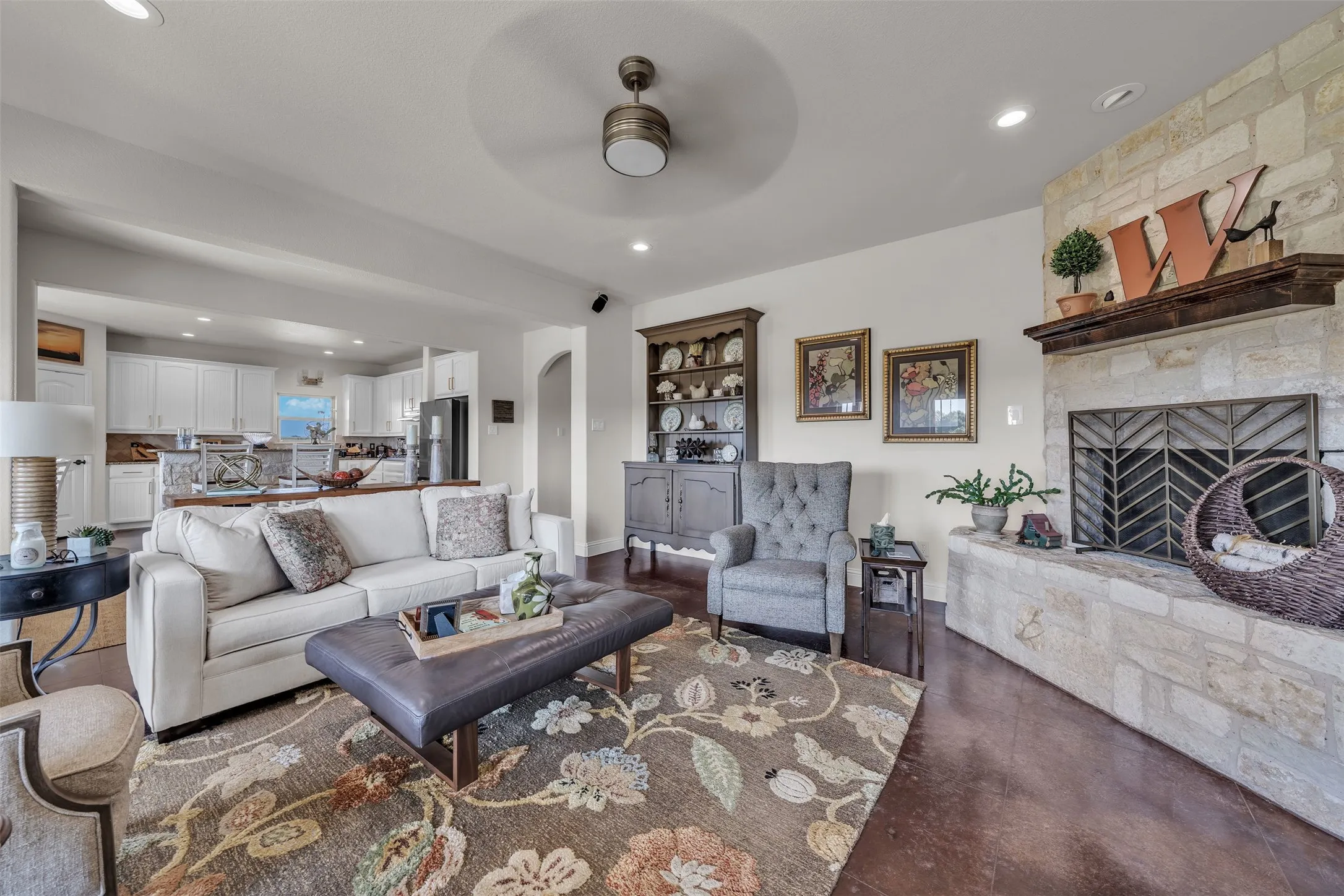 Stone-faced fireplace with a wood mantel, dark wood-finish flooring, recessed lighting, and a ceiling fan with integrated lighting