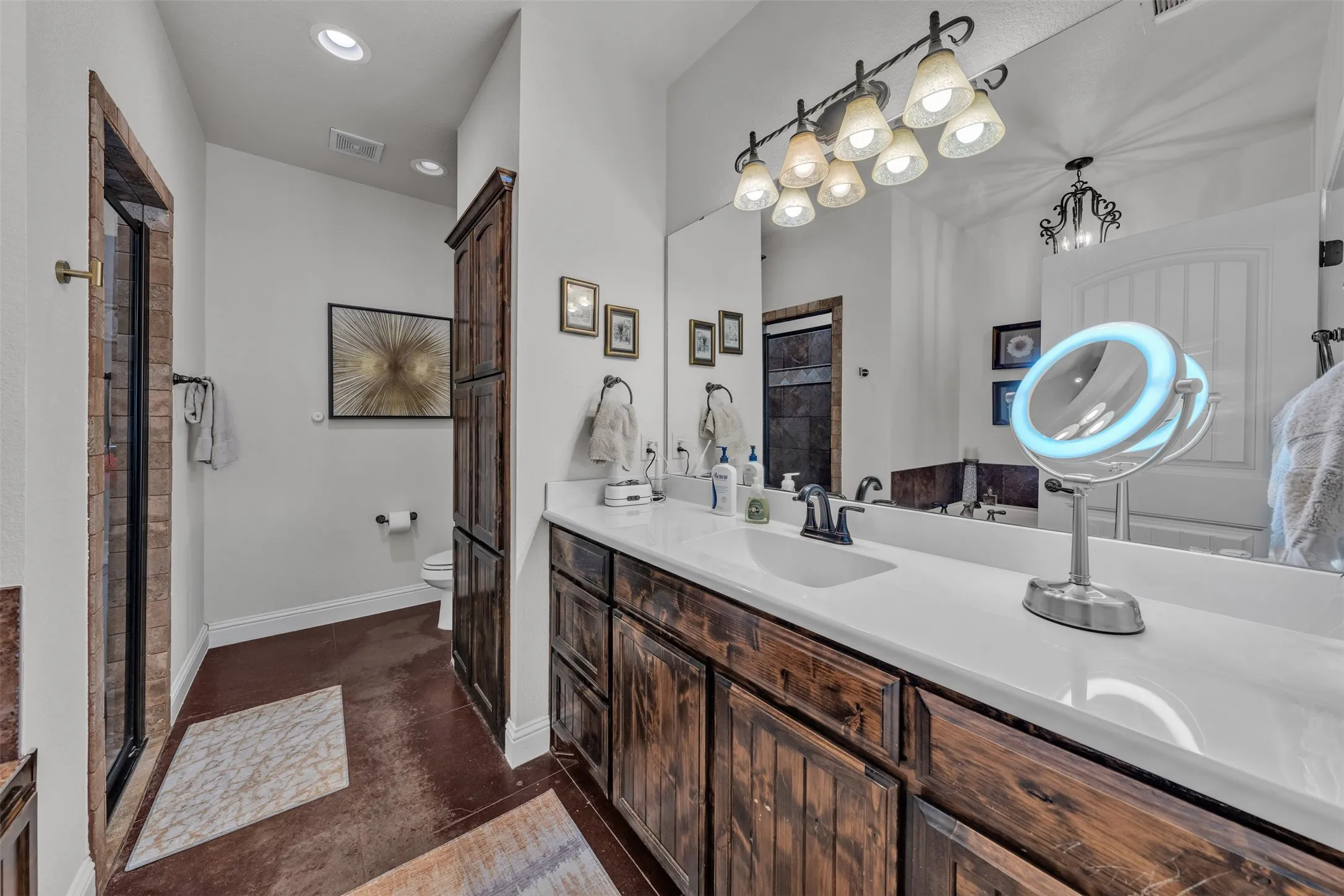 Stained wood cabinetry, white countertop, integrated sink, large vanity mirror, and recessed lighting
