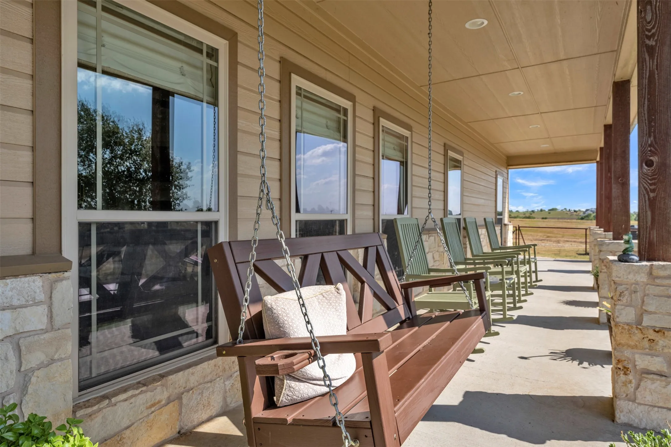Covered porch featuring a wood-slat ceiling with recessed lighting, stone column bases, and a concrete floor