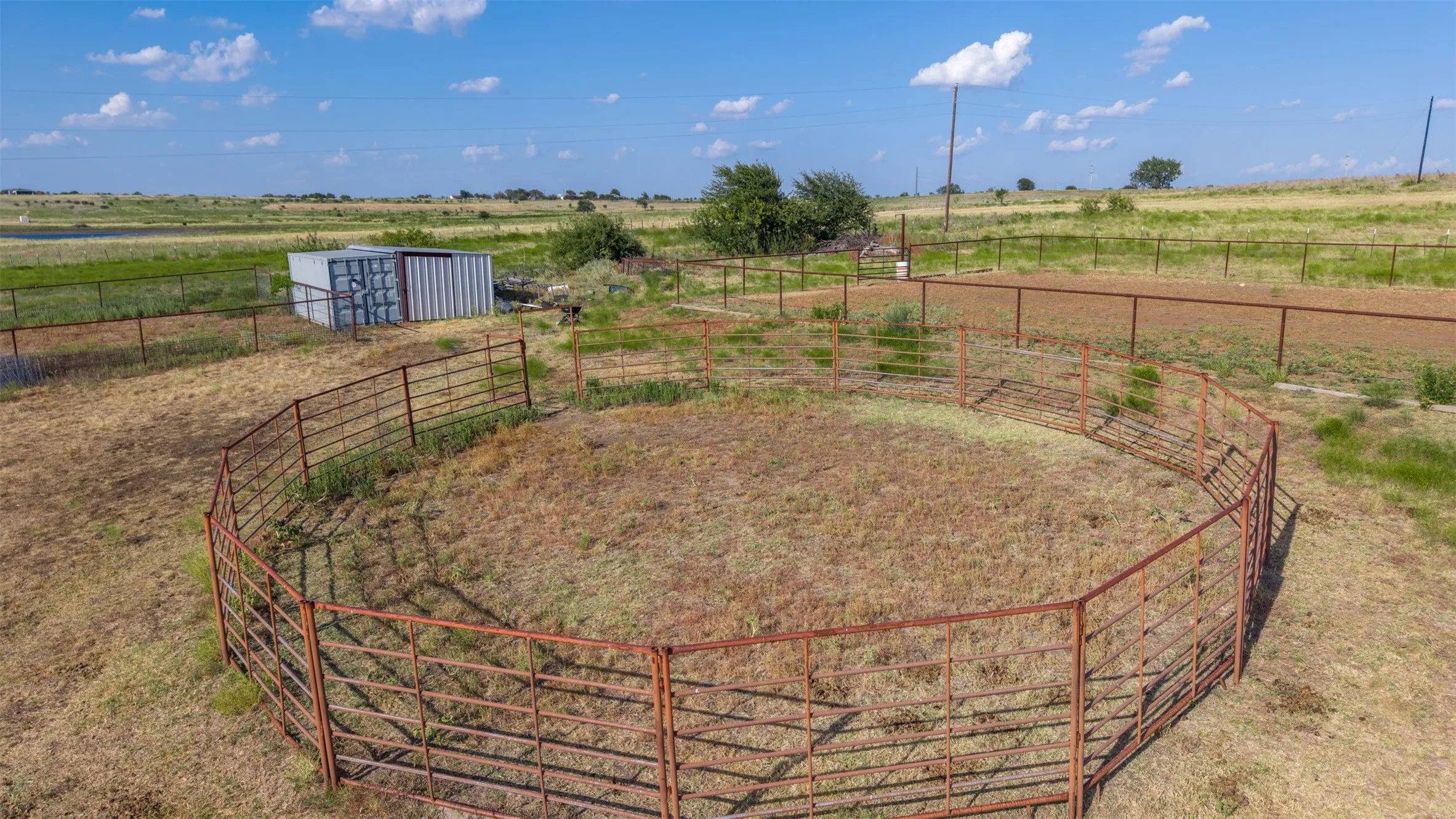 Fenced round pen with metal paneling, perimeter fencing, and a metal storage structure