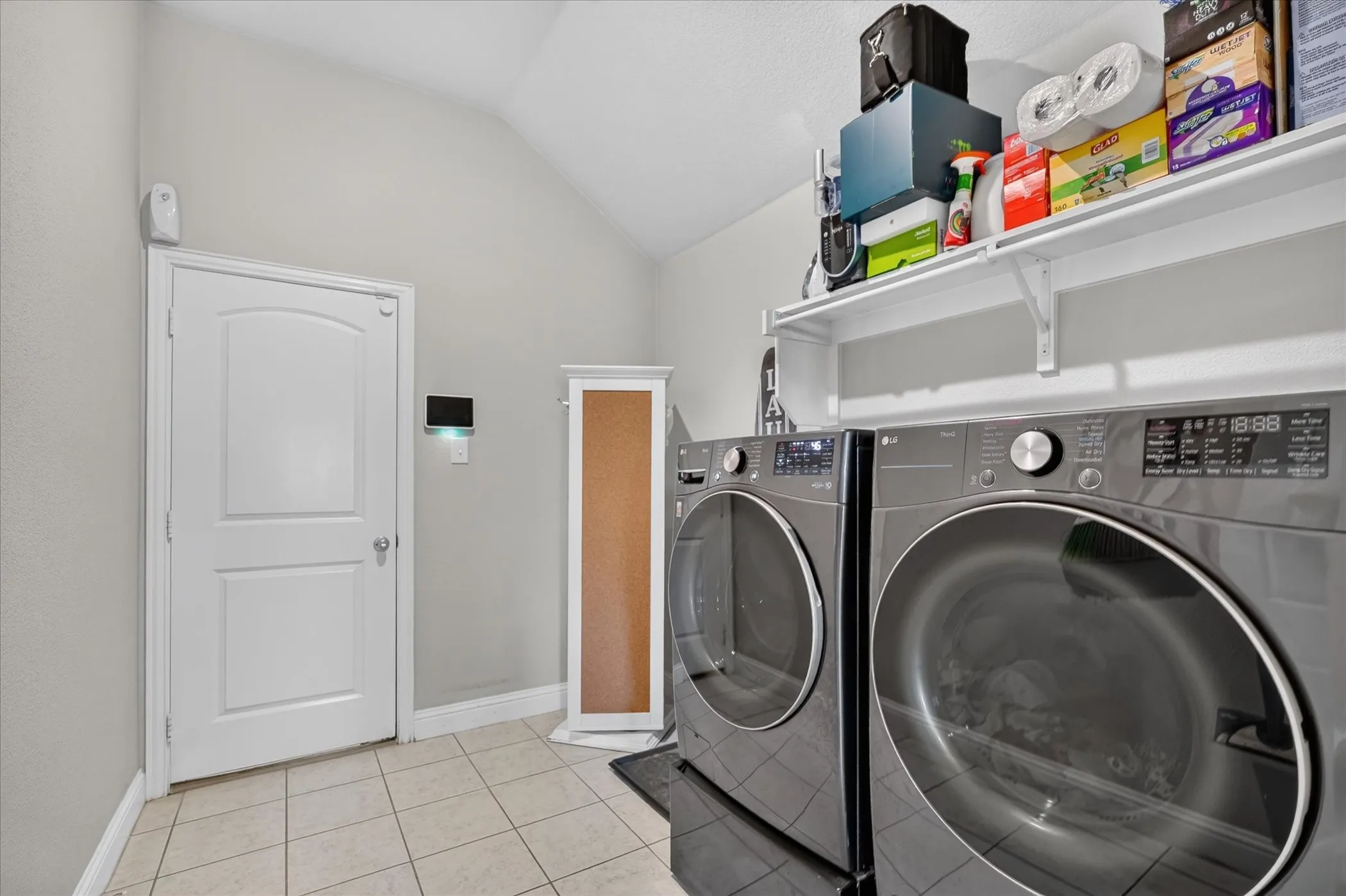 Vaulted ceiling laundry area with tile flooring and a white paneled door