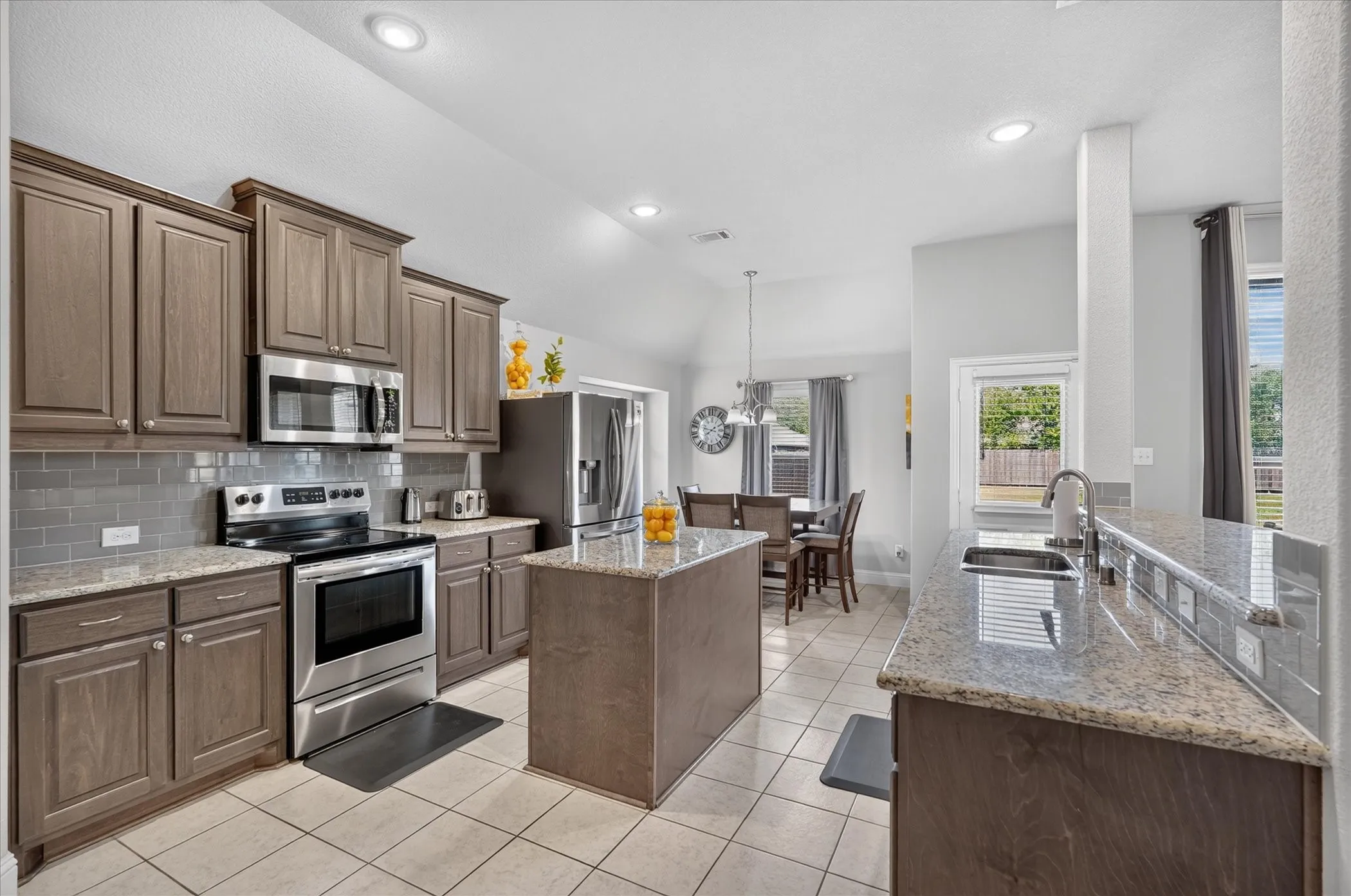 Kitchen featuring wood-finish cabinetry, stainless steel appliances, a center island with countertop, and tile flooring