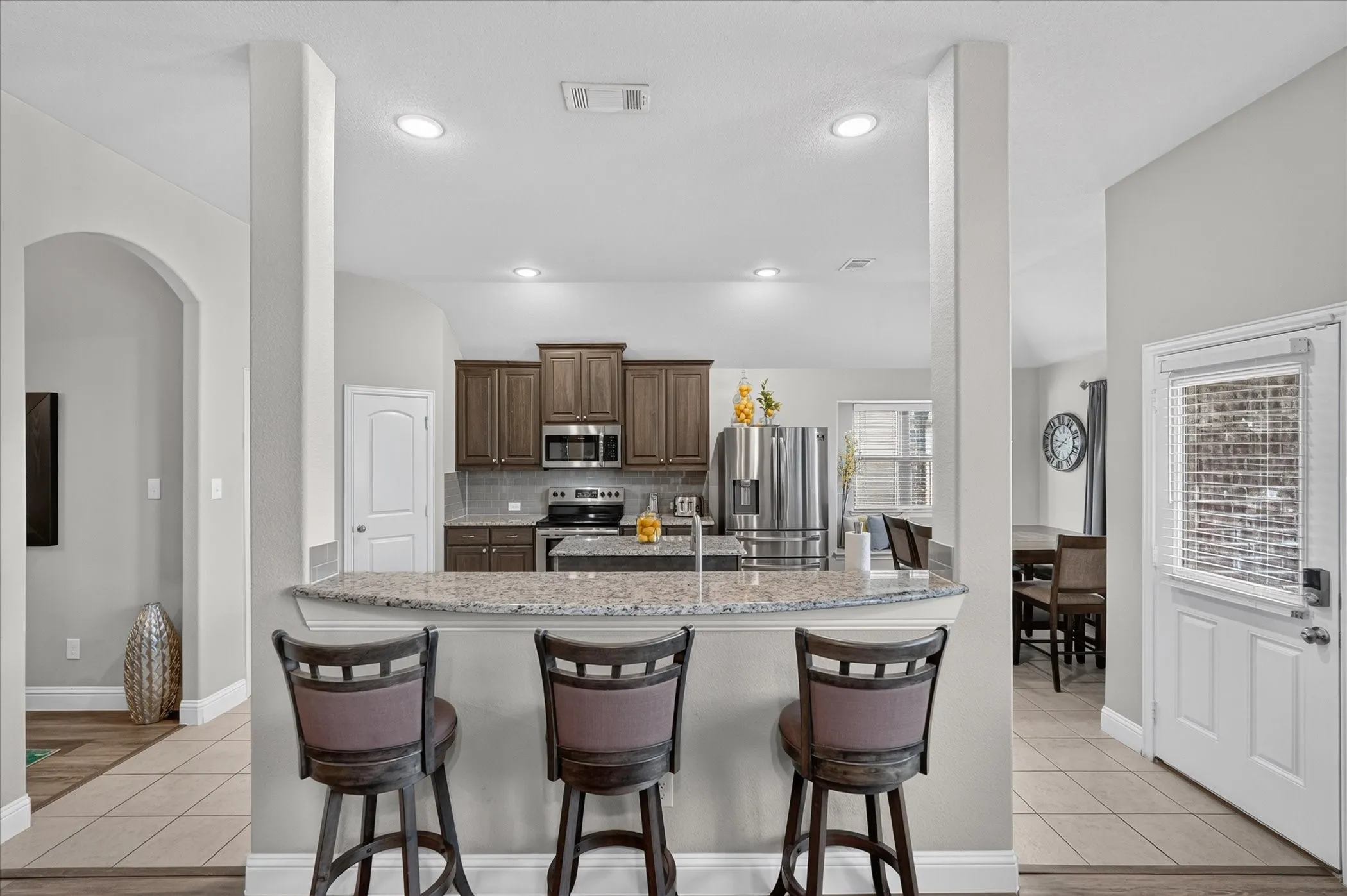 Kitchen featuring wood cabinetry, stainless steel appliances, a granite-finish breakfast bar, and recessed lighting