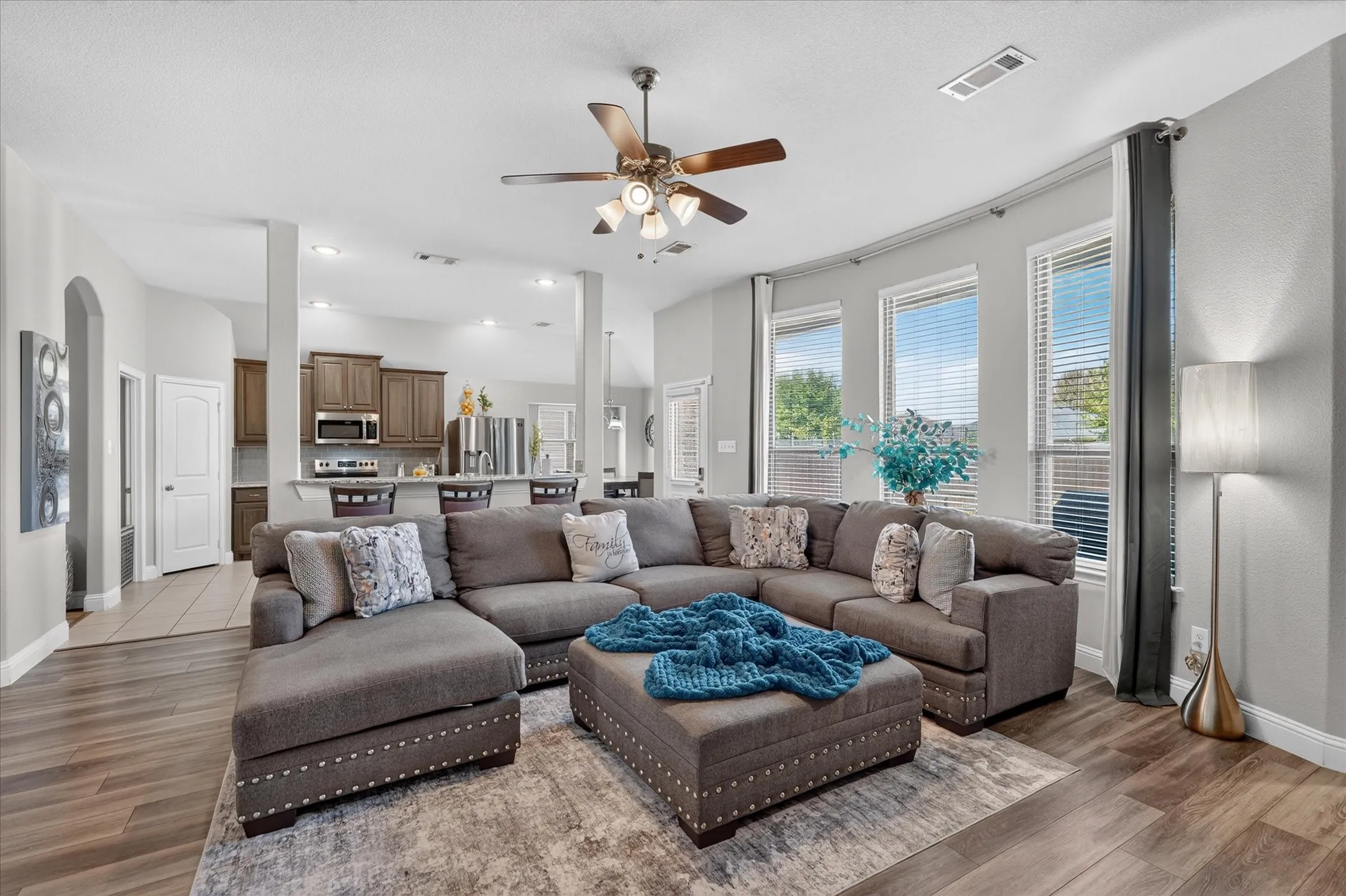 Open-concept living area featuring wood-finish flooring, recessed lighting, and multiple windows with blinds