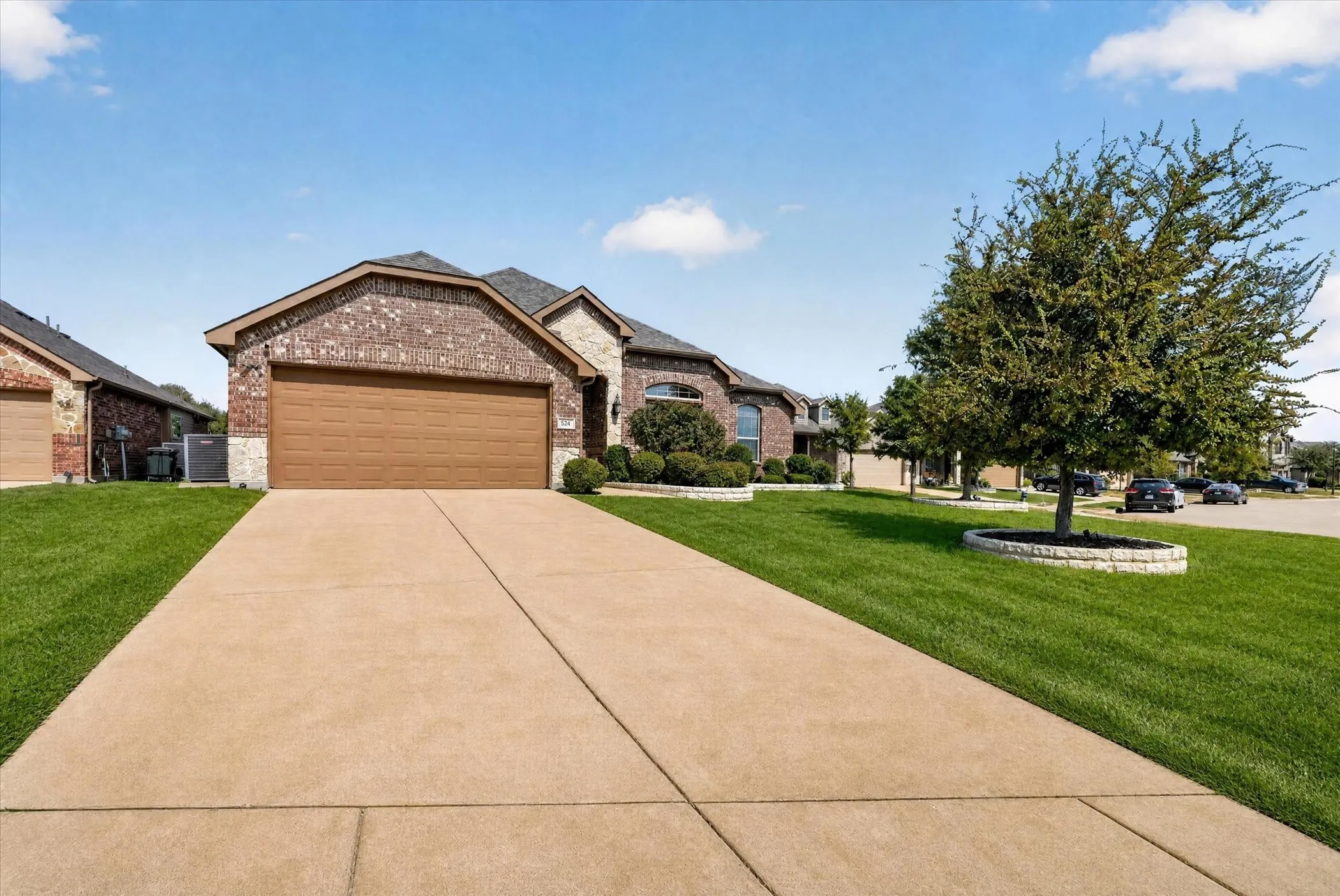 Brick exterior with stone accents, attached garage with wood-finish door, concrete driveway, and manicured lawn