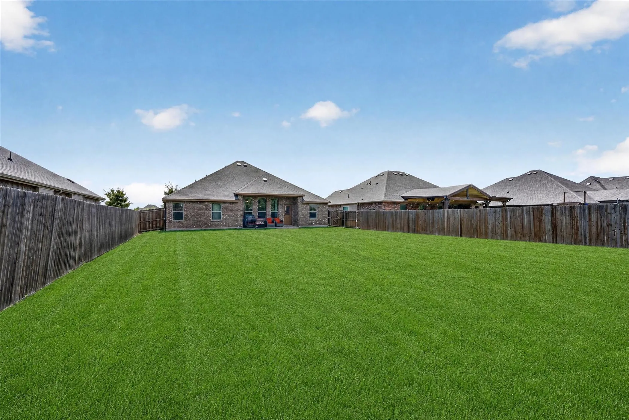 Expansive backyard featuring a manicured lawn, full perimeter fencing, and a brick-clad exterior