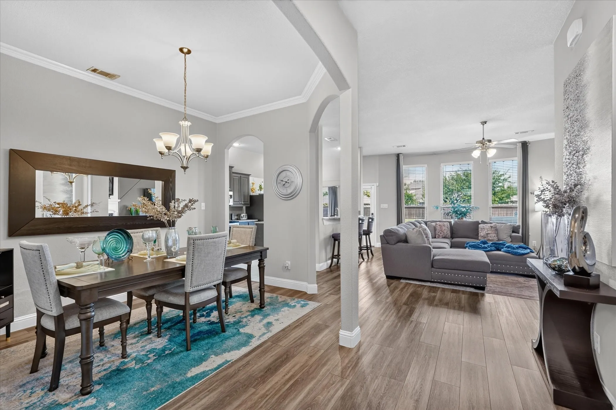 Wood-finish flooring throughout, tray ceiling with a chandelier, arched doorway, recessed lighting, and multiple windows