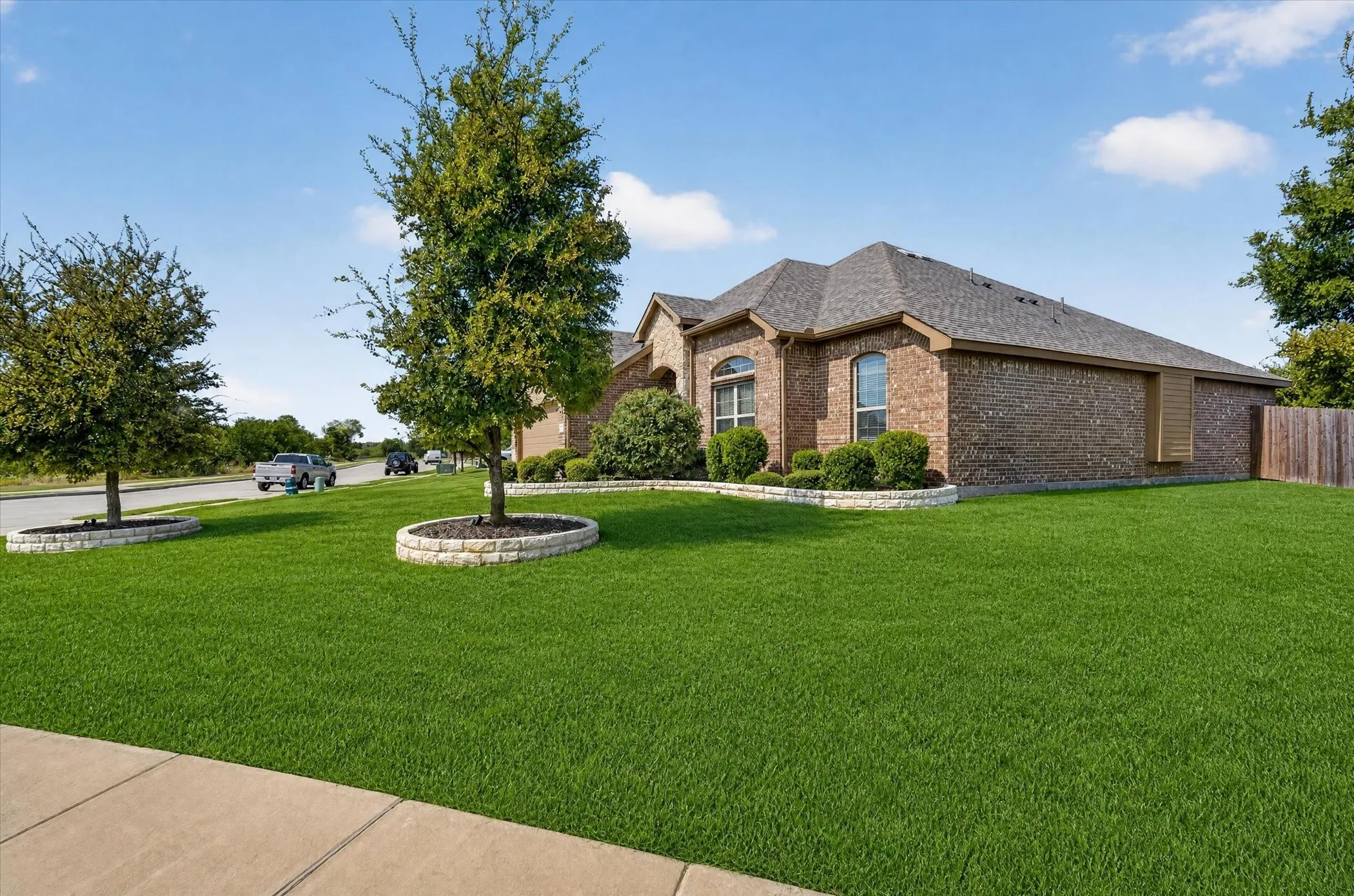 Brick exterior with arched windows, manicured lawn, established trees, and mature landscaping
