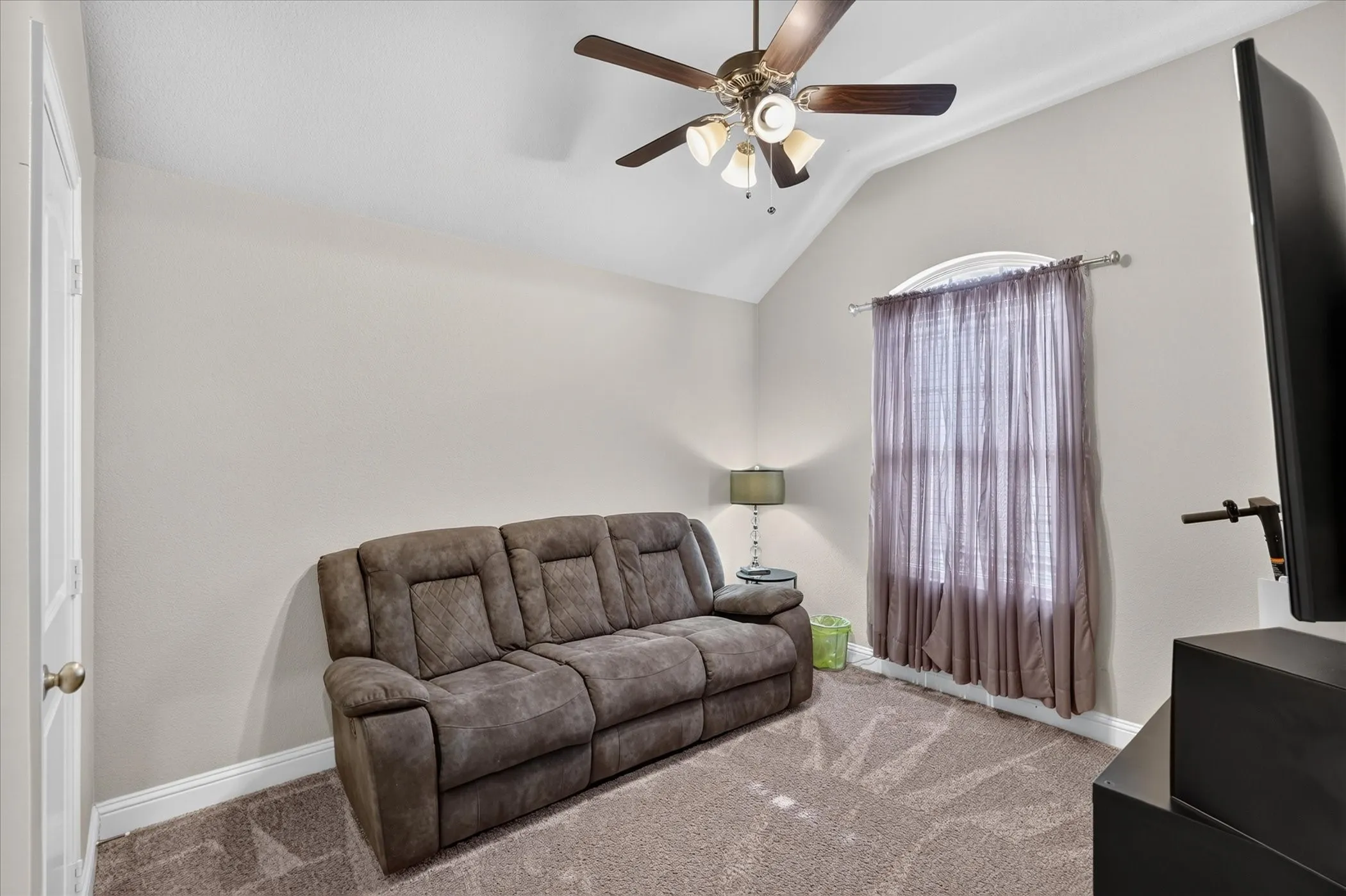 Vaulted ceiling with an integrated ceiling fan, arched window, and neutral wall tones